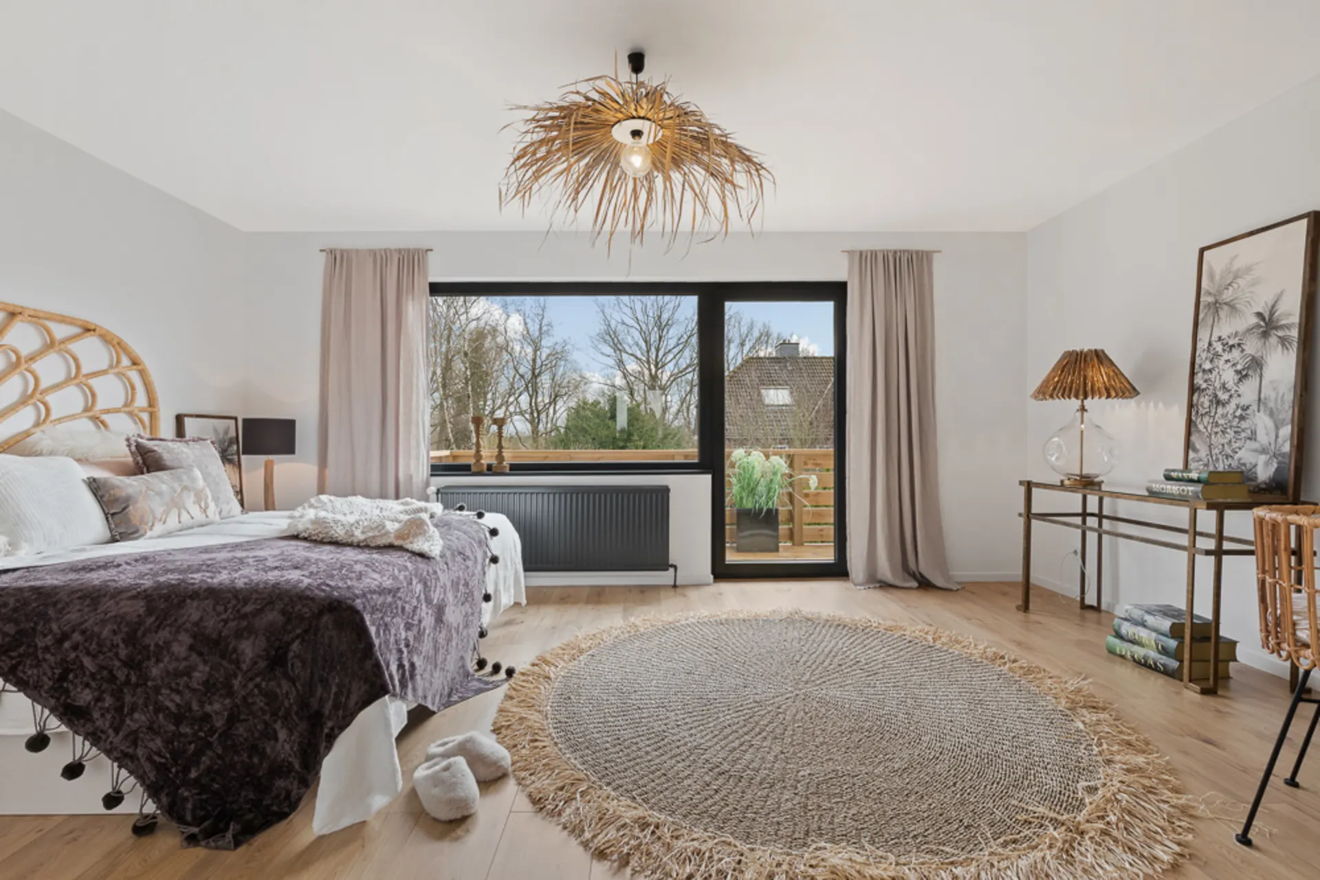 Helles Schlafzimmer mit großem Fenster, Doppelbett, rundem Teppich und Schreibtisch aus Holz.