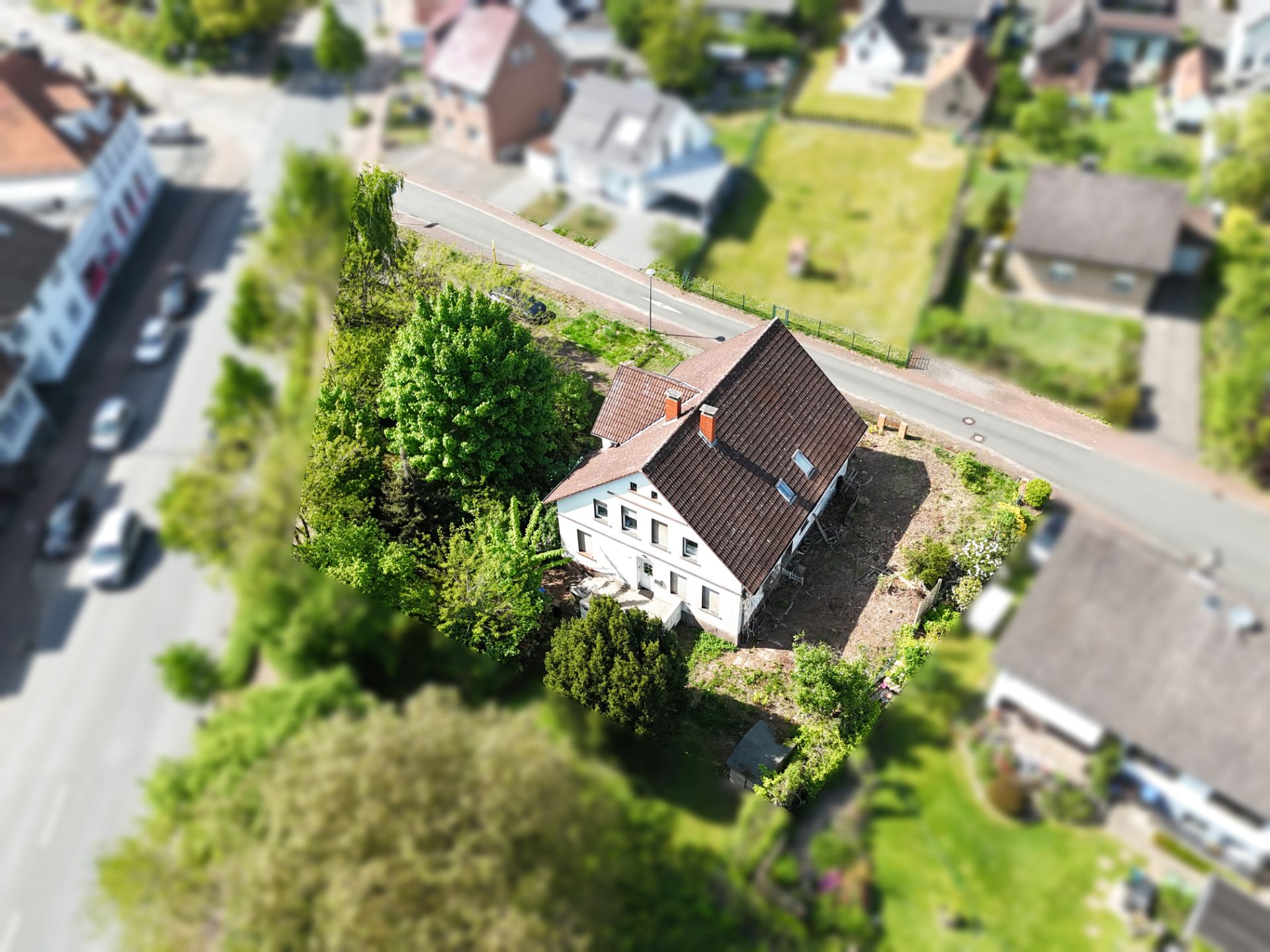 Luftaufnahme eines Einfamilienhauses mit Garten an einer Straße.