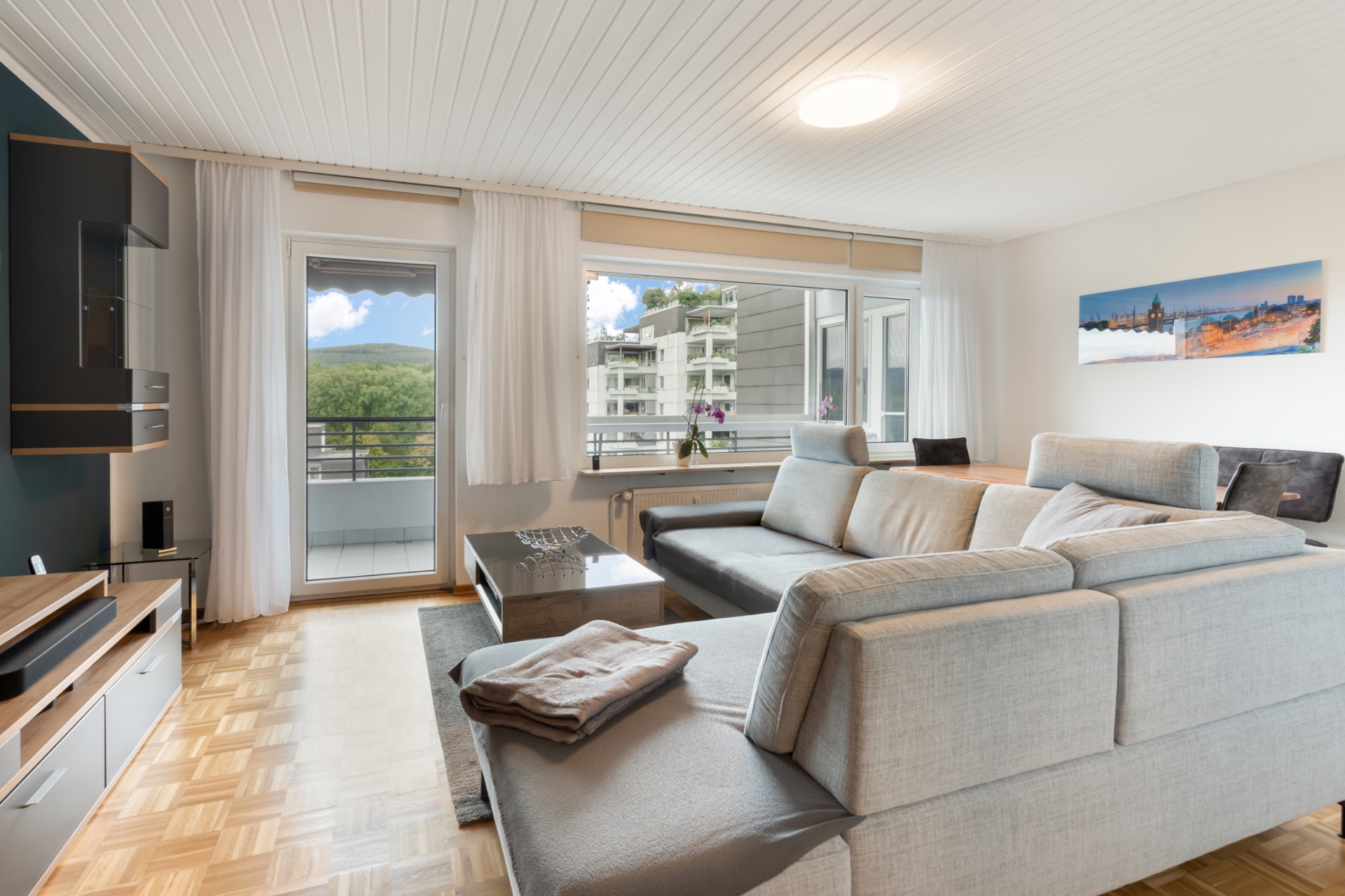 Modernes Wohnzimmer mit großer grauer Eckcouch, Couchtisch und Blick auf Balkon und Nachbargebäude.