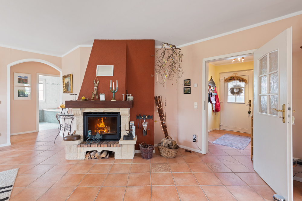 Wohnzimmer mit Kamin, offenen Türen und Fliesenboden, im Hintergrund ein Badezimmer.