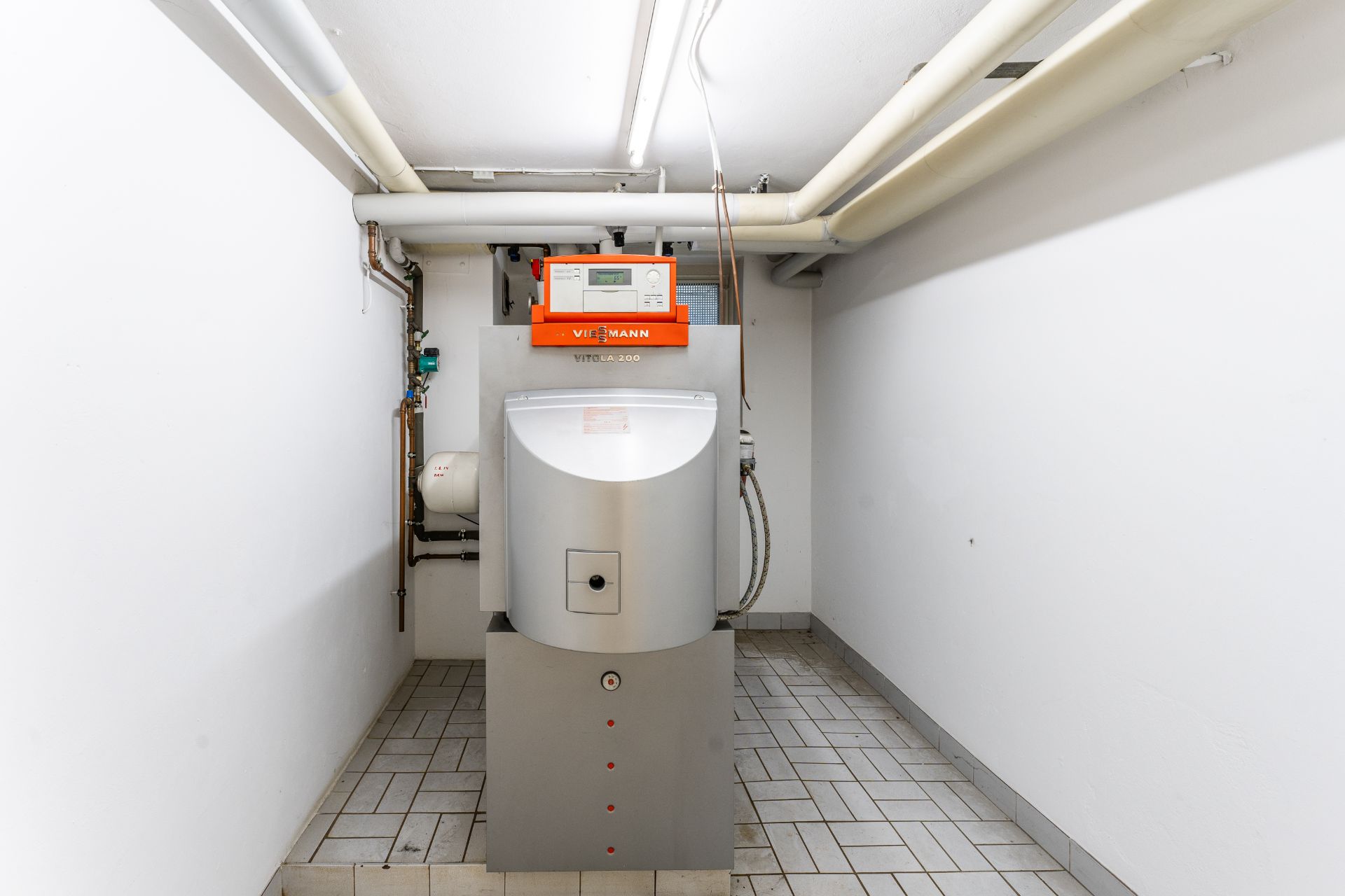 Heizungsanlage in einem weißen Kellerraum mit sichtbaren Rohren an der Decke.