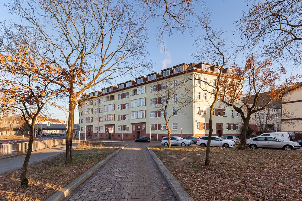 Mehrstöckiges Wohngebäude mit geparkten Autos und kahlen Bäumen im Vordergrund.