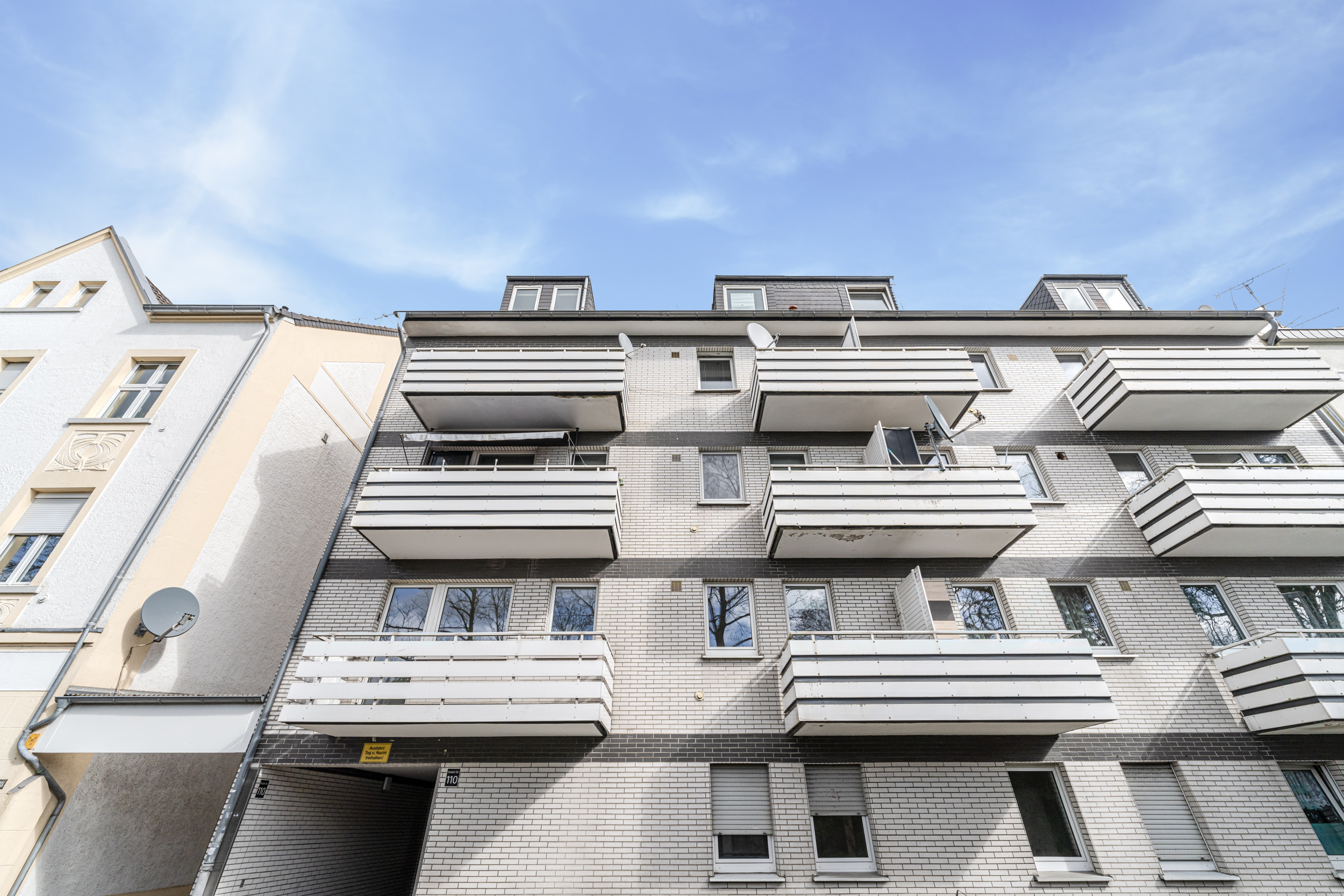 Mehrstöckiges Wohnhaus mit mehreren Balkonen und weißen Fassaden, Blick von unten.