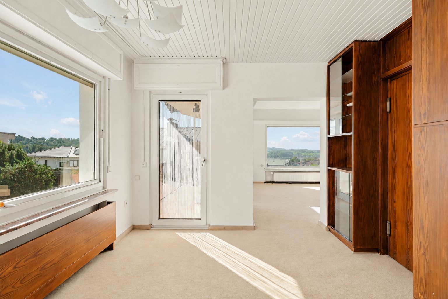 Helles Wohnzimmer mit großen Fenstern, Holzmöbeln und Blick ins Grüne.