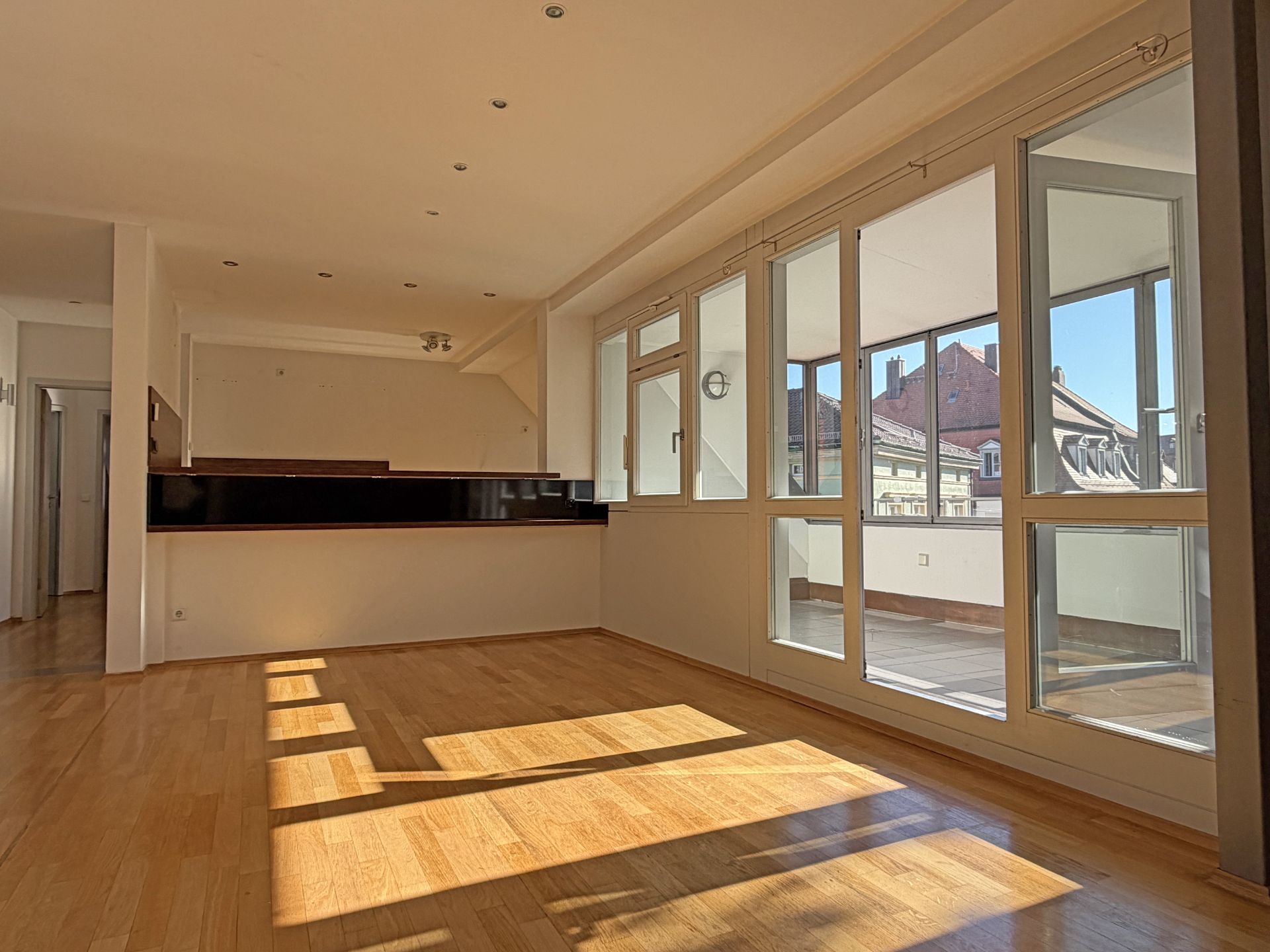 Helles Wohnzimmer mit Parkettboden, bodentiefen Fenstern und Zugang zu einem Balkon.