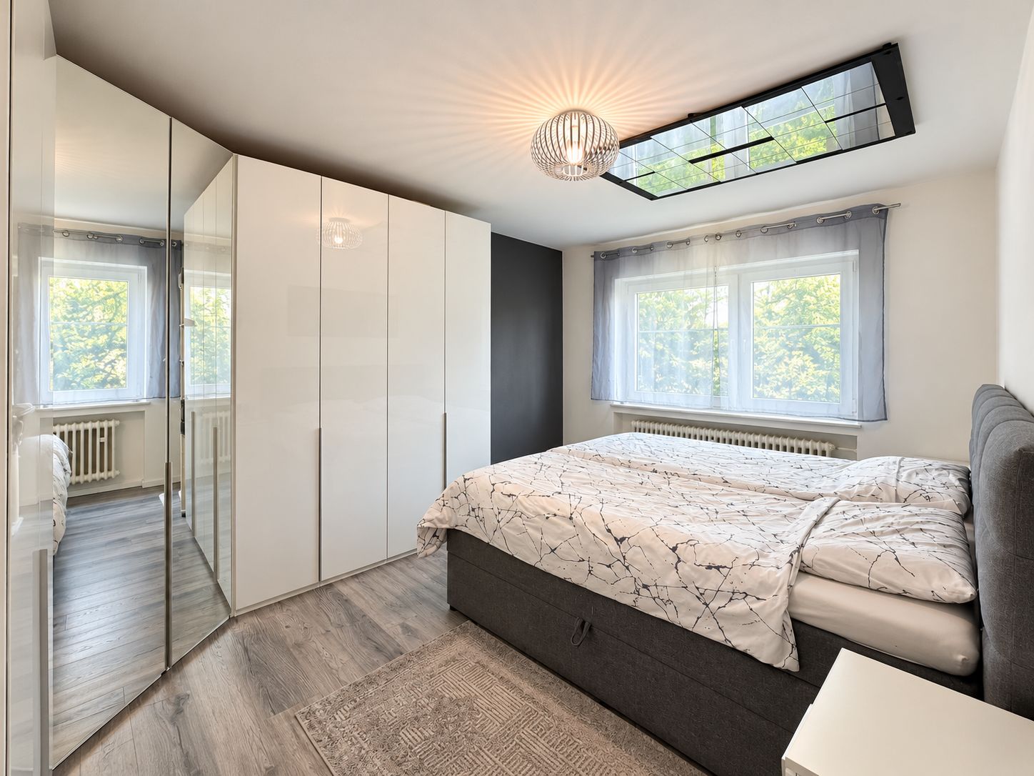 Helles Schlafzimmer mit großem Bett, weißem Kleiderschrank und zwei Fenstern.