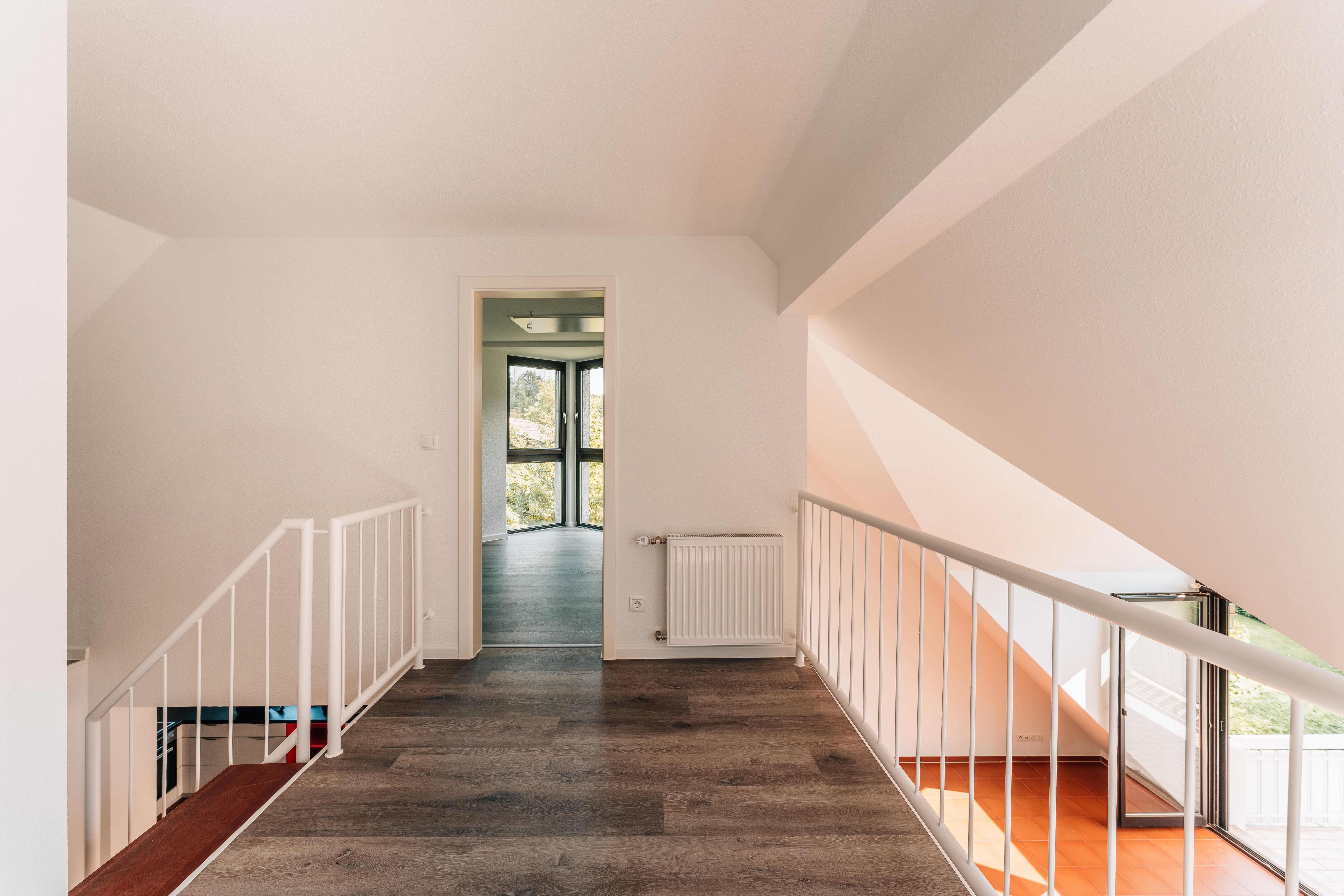 Heller Flur mit Holzfußboden und Treppengeländer, Blick auf Fenster und Zimmer.