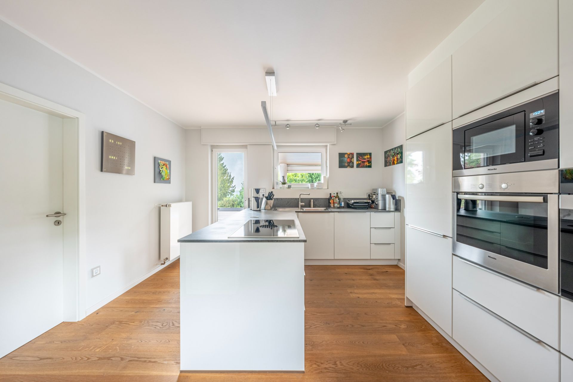 Moderne helle Küche mit Kochinsel, weißen Schränken und Holzboden.
