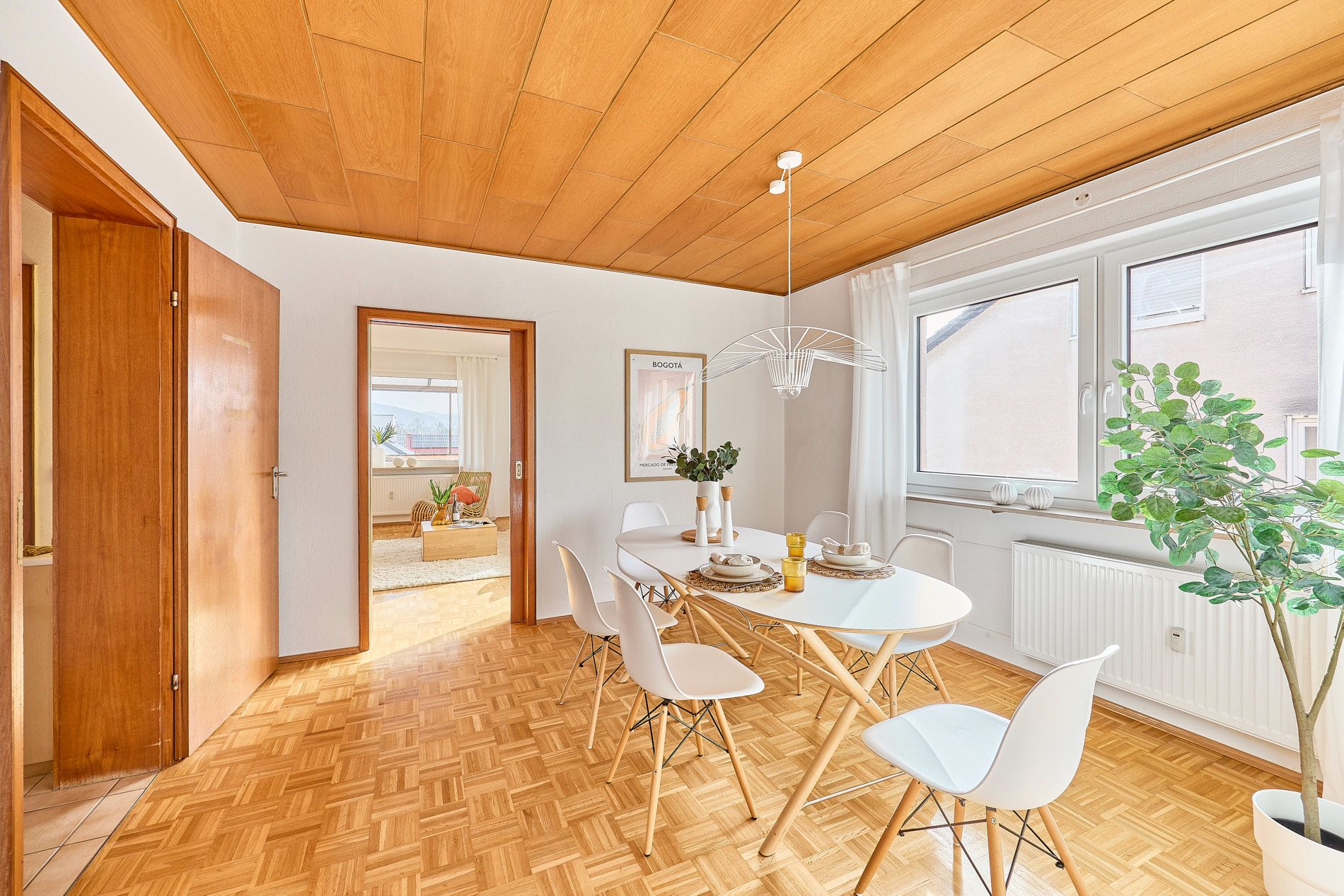 Heller Essbereich mit weißem Tisch, sechs Stühlen und großen Fenstern, Holzboden und Holzdecke.