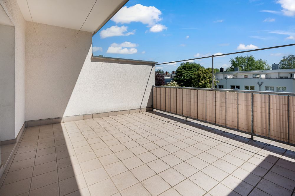 Großer, gefliester Balkon mit Geländer und Blick auf Bäume und benachbarte Gebäude.