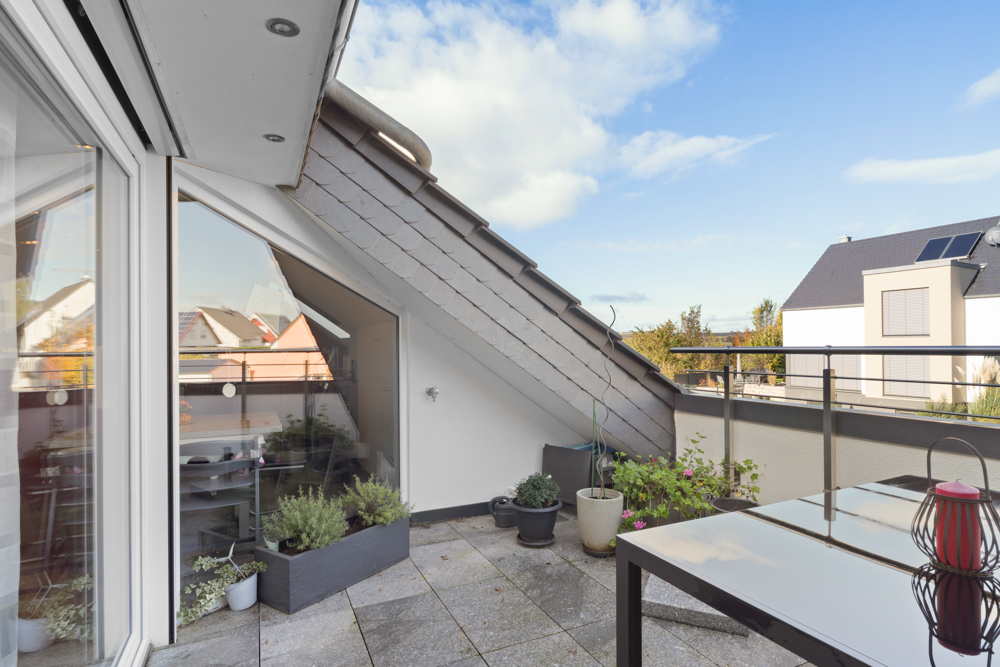 Dachterrasse mit Esstisch, Blumenkübeln und Blick auf Nachbarhäuser bei Tageslicht.