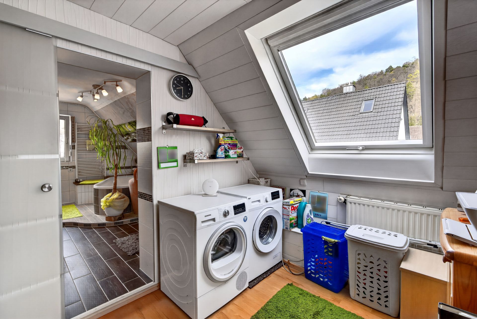 Waschraum mit Waschmaschine, Trockner, Dachfenster und Regalen mit Haushaltsartikeln.