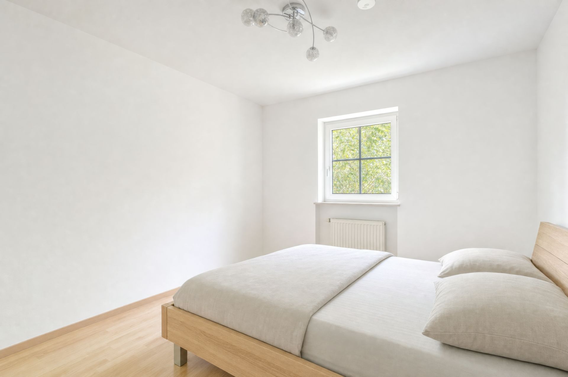 Helles Schlafzimmer mit Holzbett, zwei Kissen und Fenster mit Blick ins Grüne.