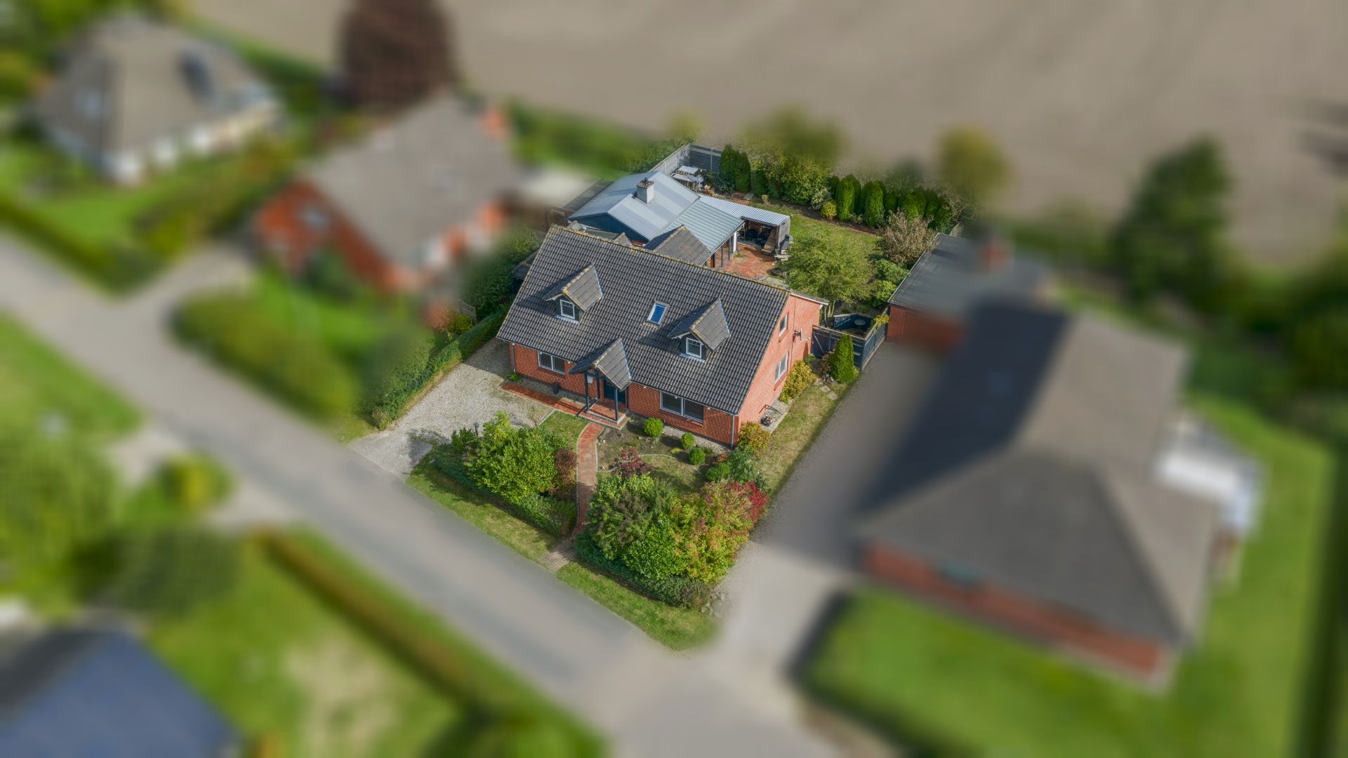 Luftaufnahme eines Hauses mit Garten, umgeben von weiteren Häusern und einer Straße.