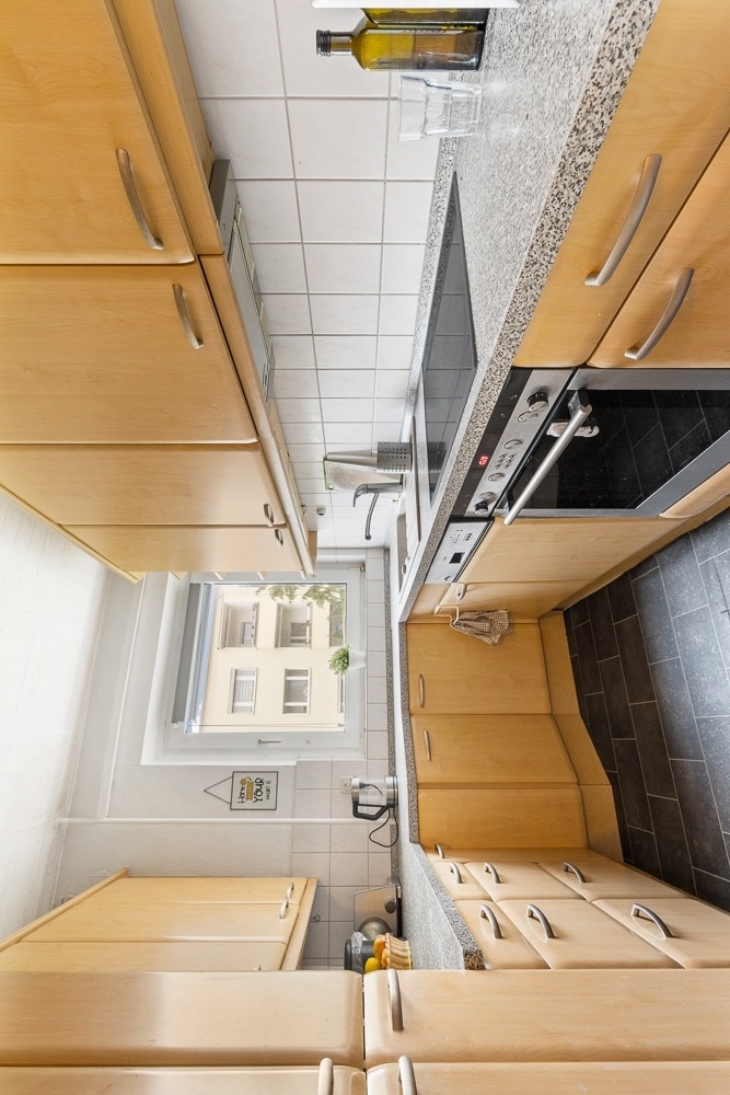 Moderne Küche mit hellen Holzschränken, Elektroherd, Spüle und Fenster mit Blick nach draußen.