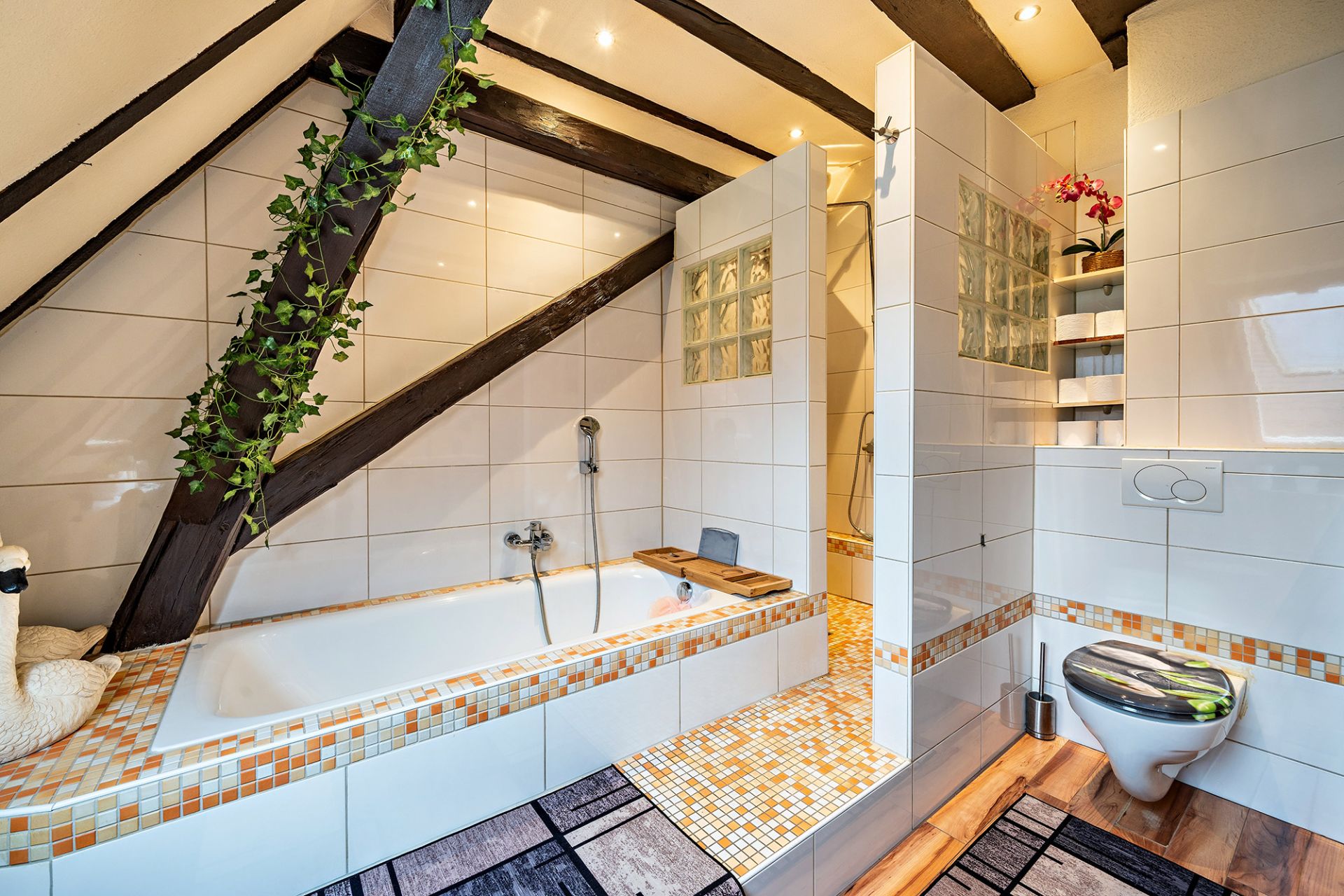 Modernes Badezimmer mit Badewanne, Dusche, WC und Dachbalken. Fliesen in Weiß und Orange.