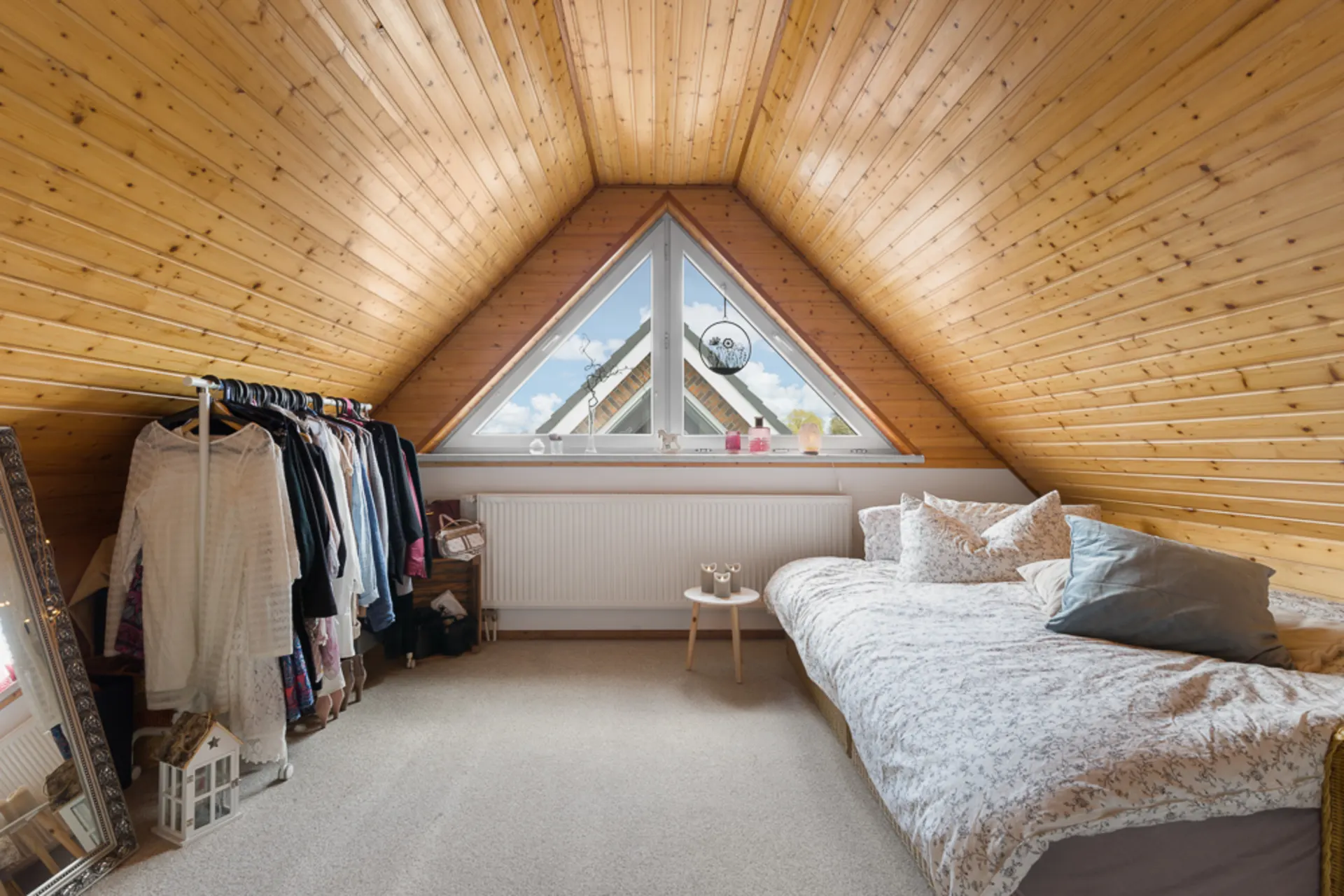 Gemütliches Zimmer mit Holzverkleidung, Bett, Fenster, Kleiderständer und großem Spiegel.