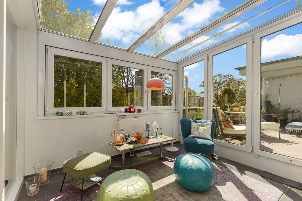 Heller Wintergarten mit Glastür, Sitzgelegenheiten, Teppich und Blick auf die Terrasse.