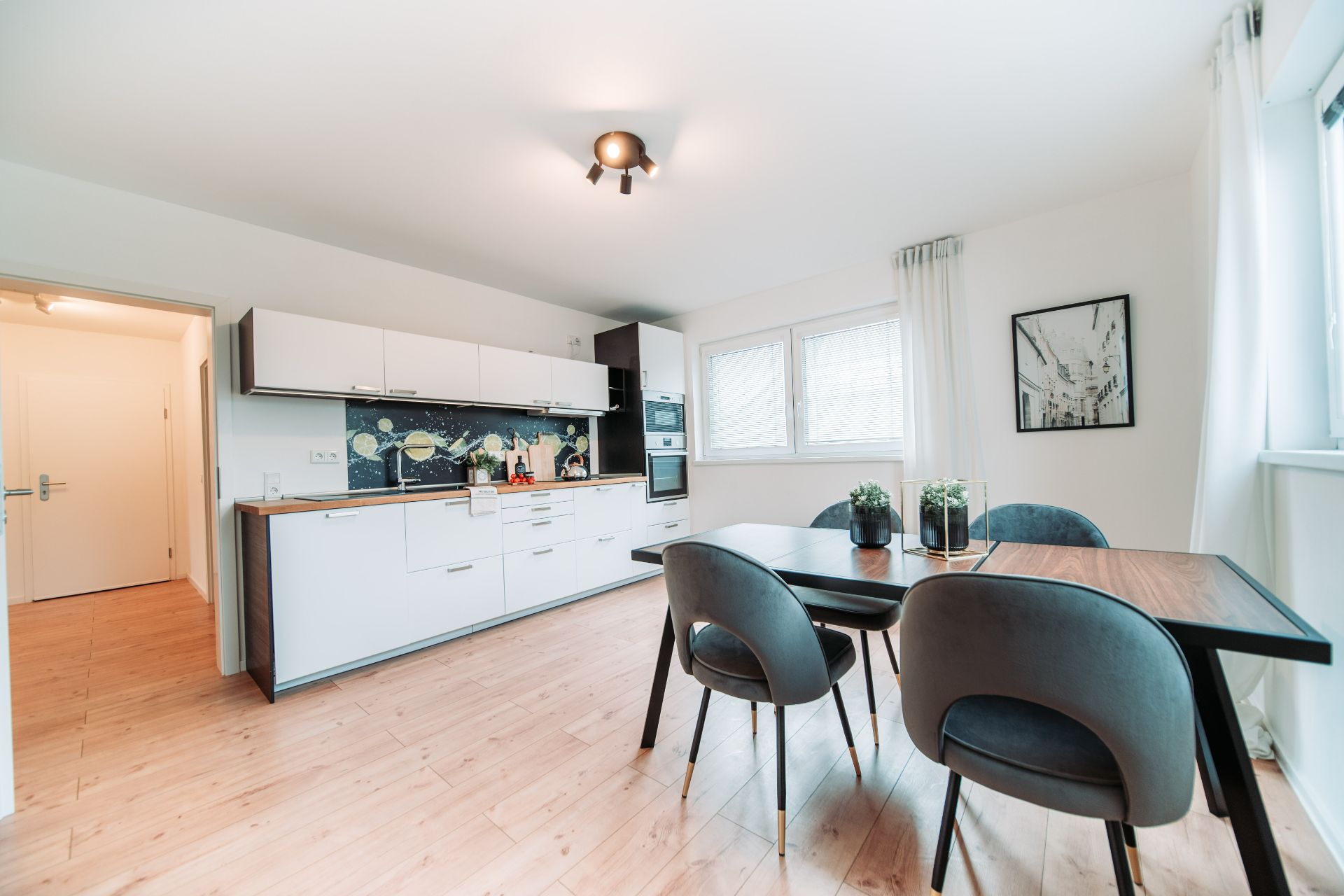 Moderne offene Küche mit Essbereich, Holzboden, Tisch mit vier Stühlen und großen Fenstern.