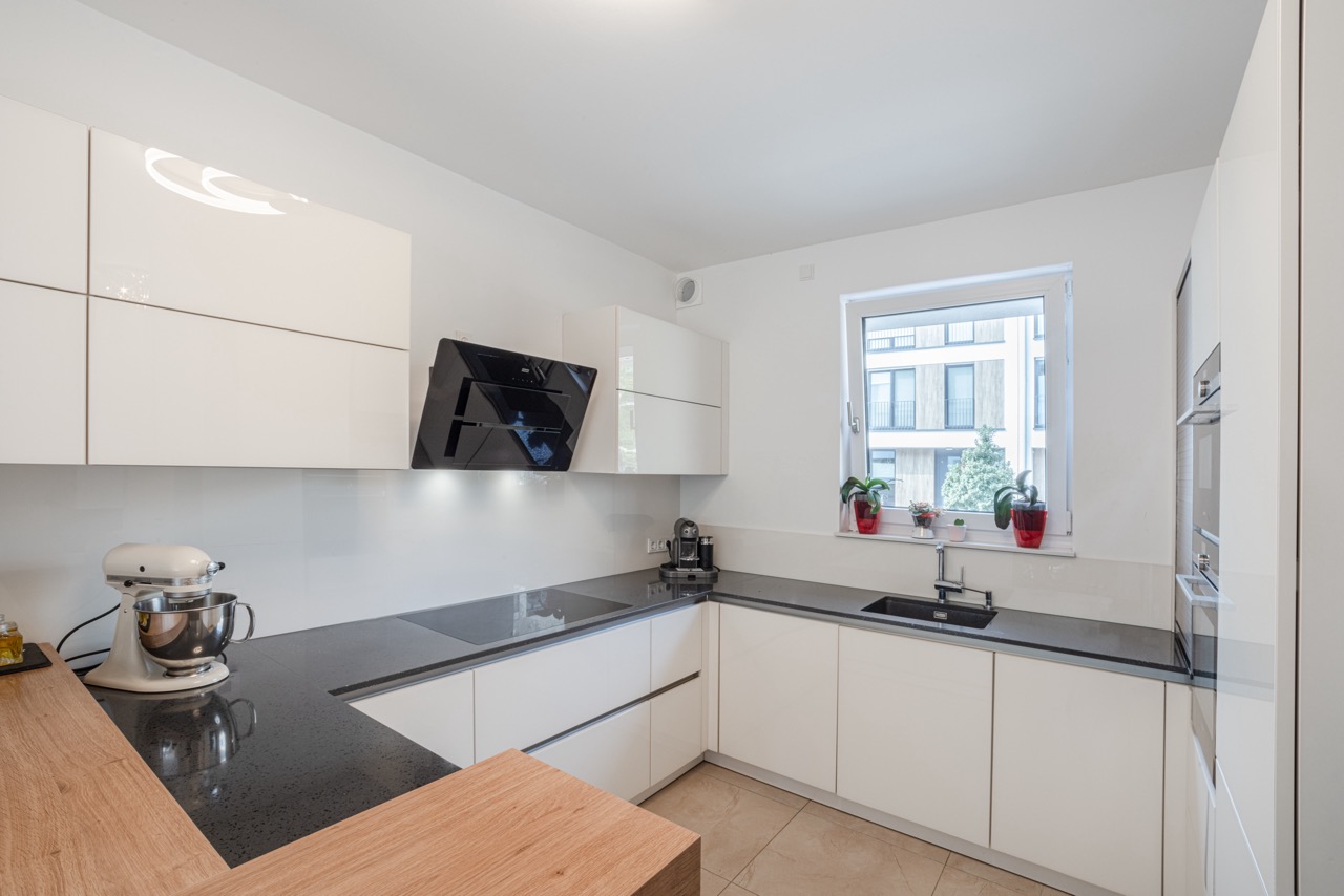 Moderne weiße Einbauküche mit Fenster, Pflanzen und Küchenmaschinen auf der Arbeitsplatte.
