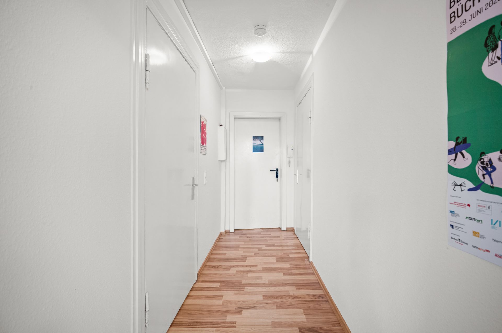 Heller Flur mit Holzboden, weißen Wänden und mehreren Türen zu Wohnräumen.