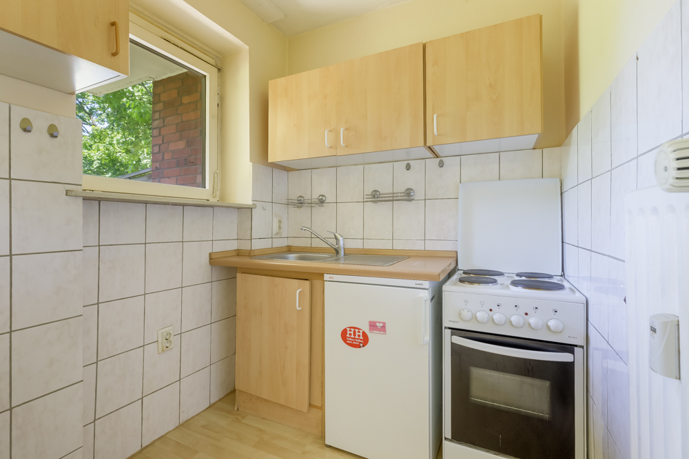 Kleine Küche mit Fenster, Spüle, Kühlschrank, Herd und Holzschränken.