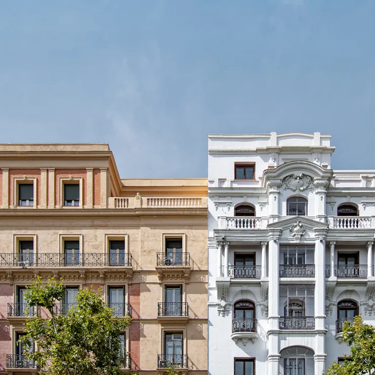 Fassade zweier historischer Wohngebäude mit Balkonen und Bäumen davor.
