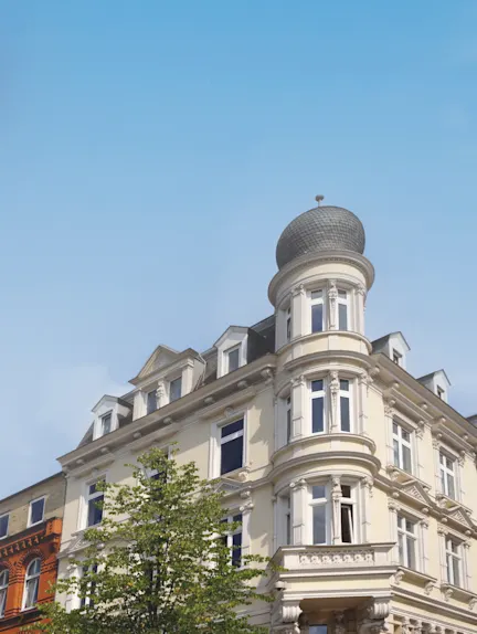 Altbau-Wohnhaus mit Türmchen und vielen Fenstern vor blauem Himmel.