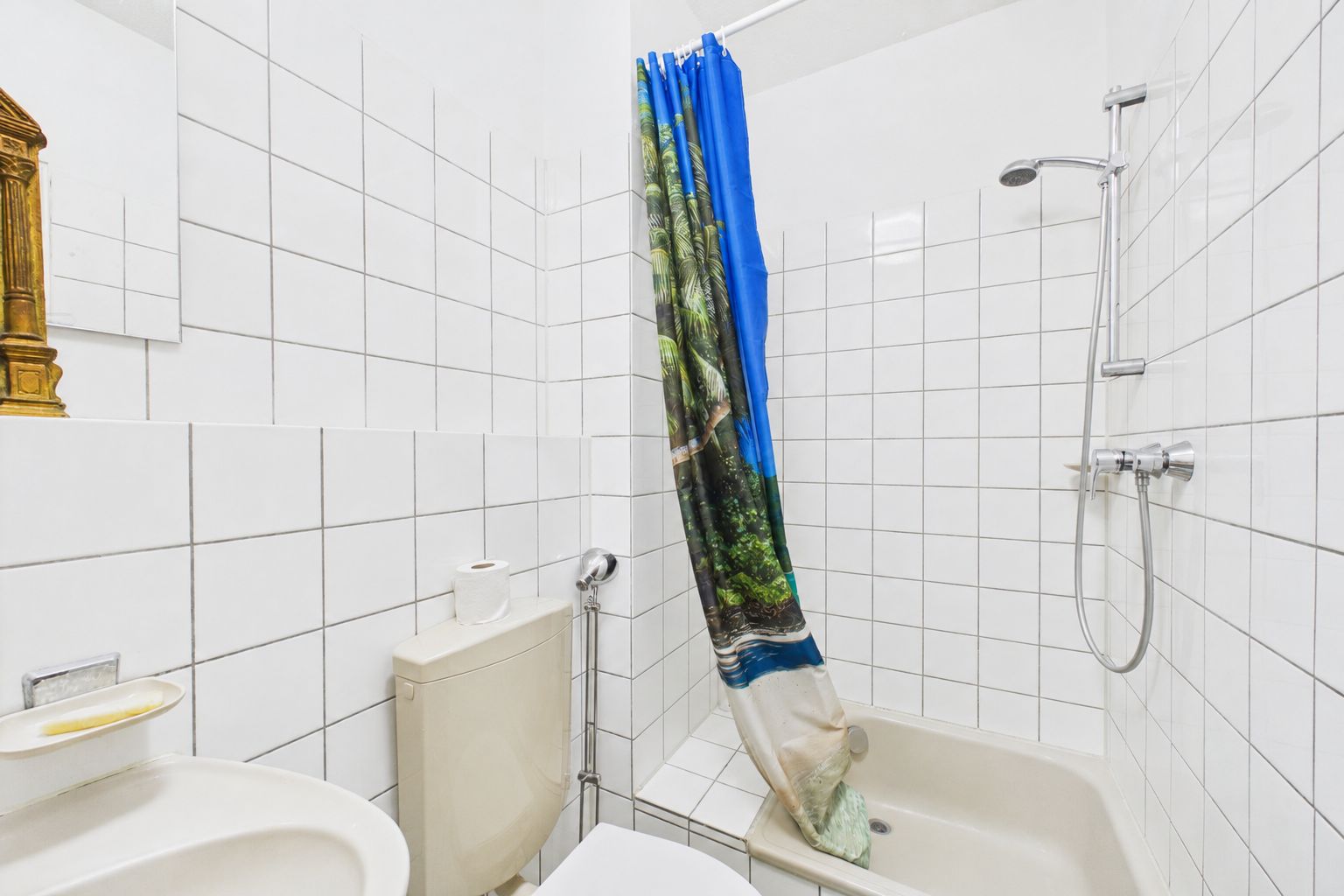 Kleines Badezimmer mit Dusche, WC, Waschbecken und Duschvorhang mit Naturmotiv.