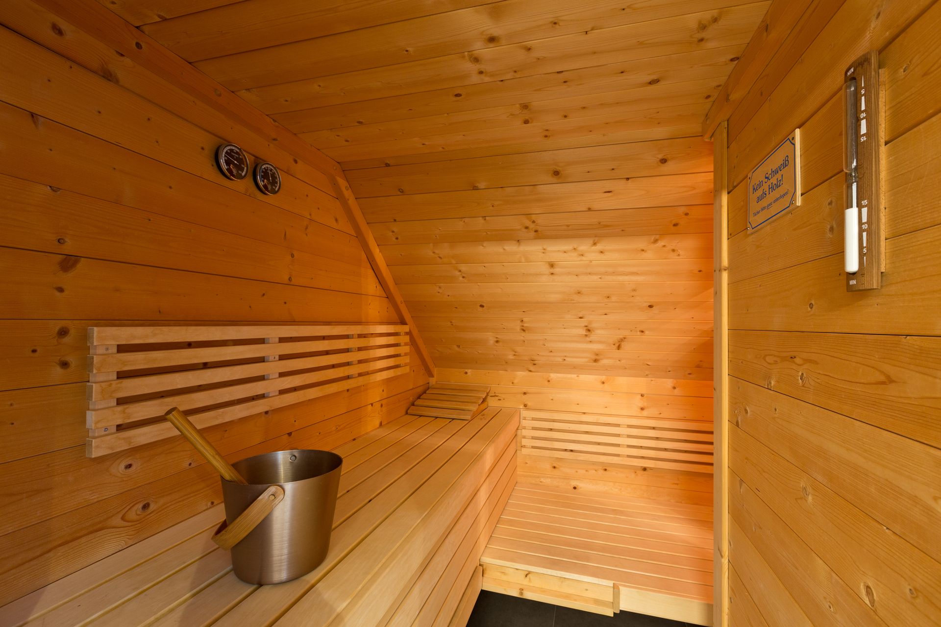 Holzsauna mit Bank, Aufgusseimer und Thermometern an der Wand.