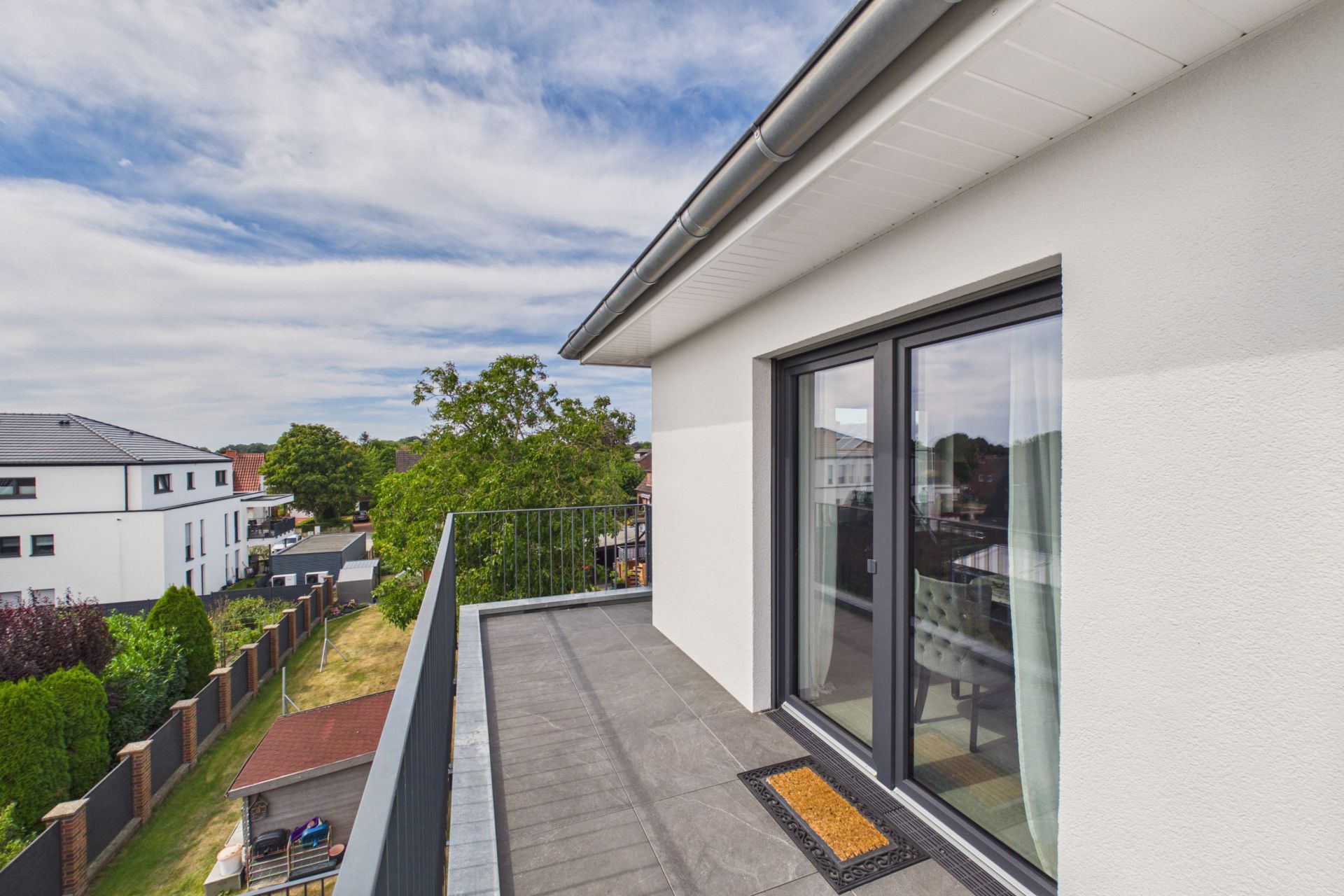 Moderner Balkon mit Glasgeländer und Blick auf Nachbarhäuser und Garten.