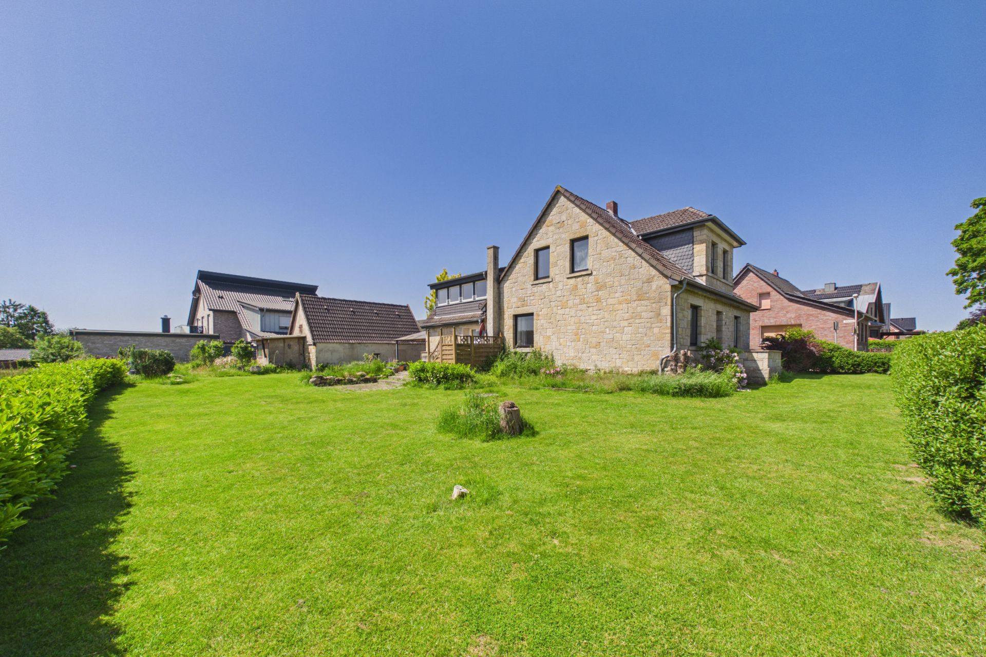 Ein Einfamilienhaus mit großem Garten und Wiese, umgeben von anderen Häusern bei klarem Himmel.