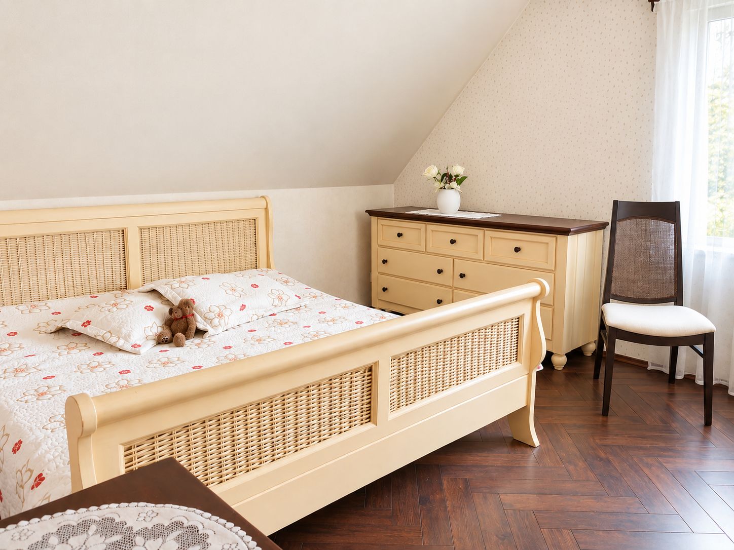 Gemütliches Schlafzimmer mit cremefarbenem Bett, Kommode, Stuhl und Tageslicht am Fenster.