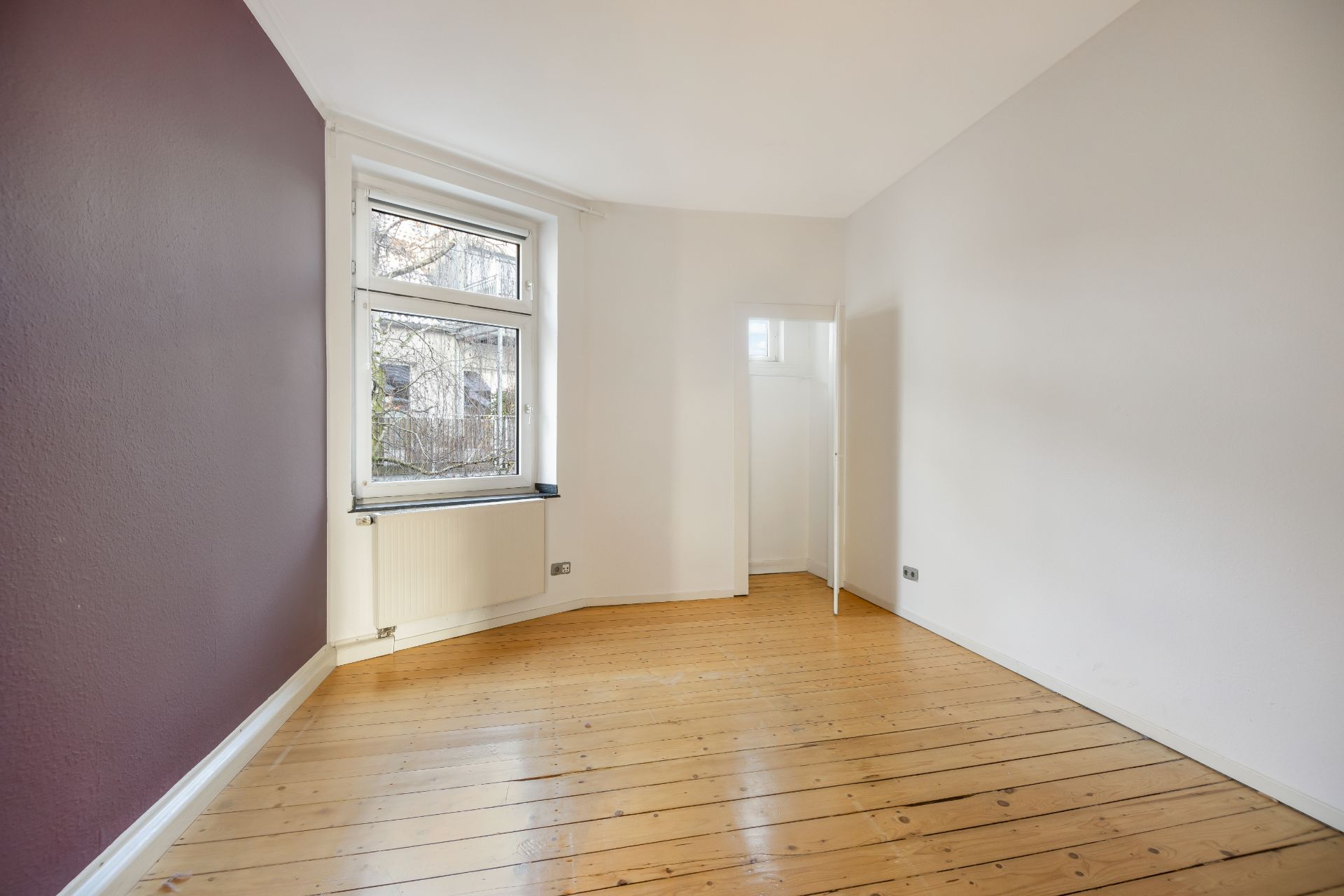 Leerer Raum mit Holzboden, einem Fenster und einer lila und weißen Wand.