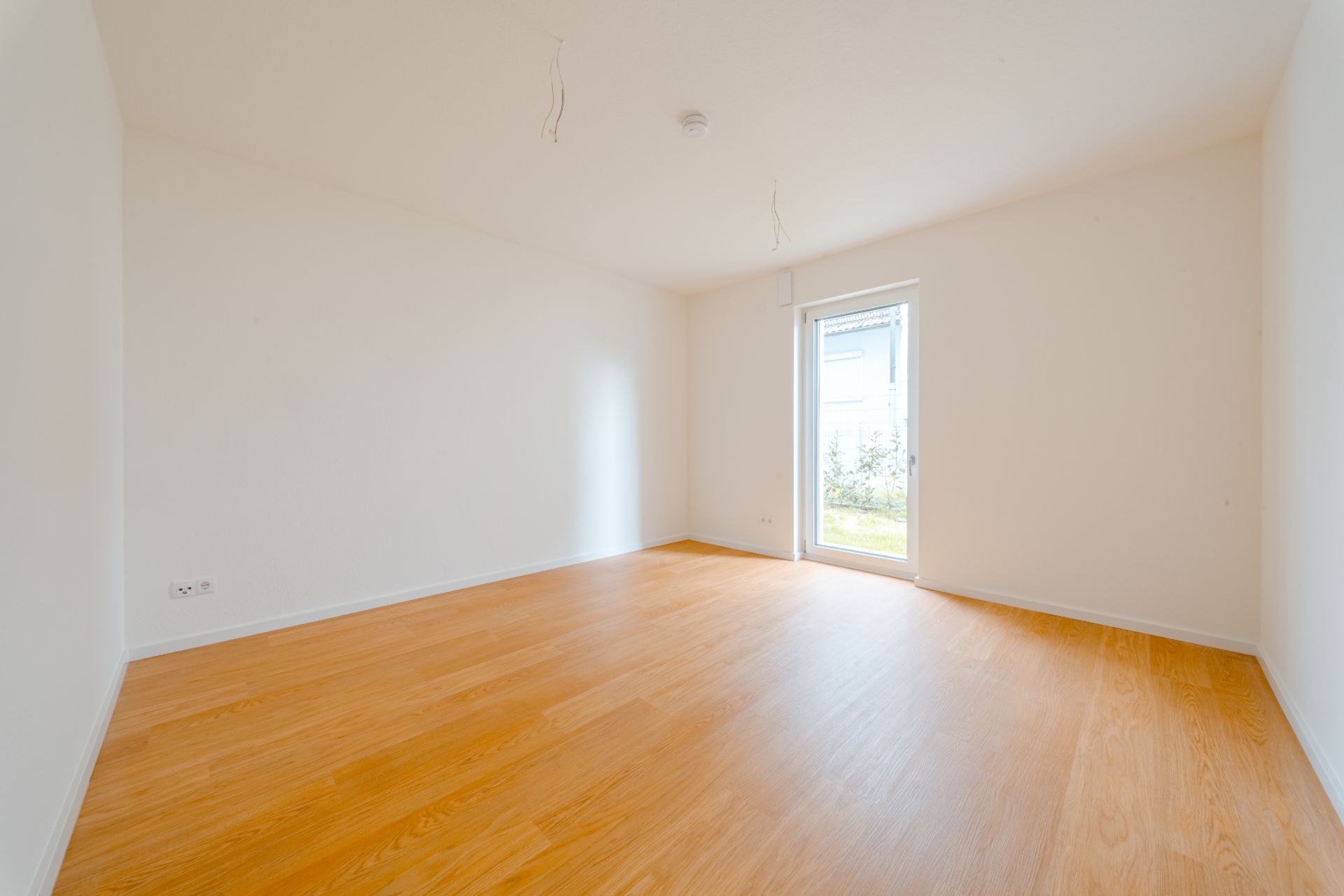 Leerer Raum mit Holzfußboden, weißen Wänden und einer Glastür nach draußen.