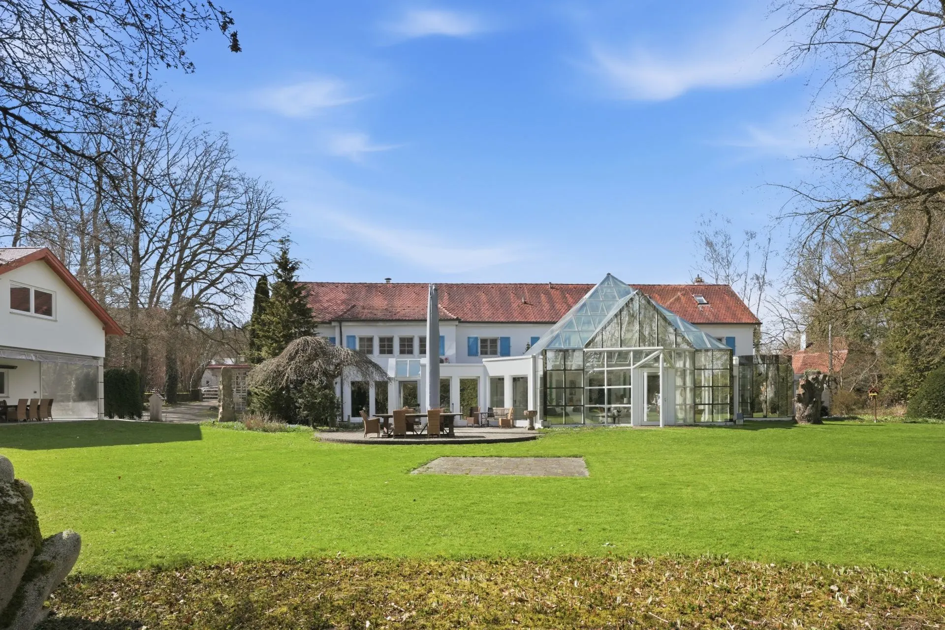 Großes Wohnhaus mit Wintergarten und großer grüner Rasenfläche im Vordergrund.