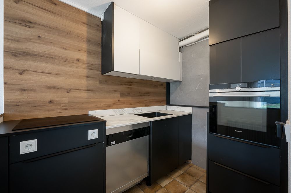 Moderne Küche mit schwarzen Schränken, Holzrückwand, Herd und eingebautem Ofen.