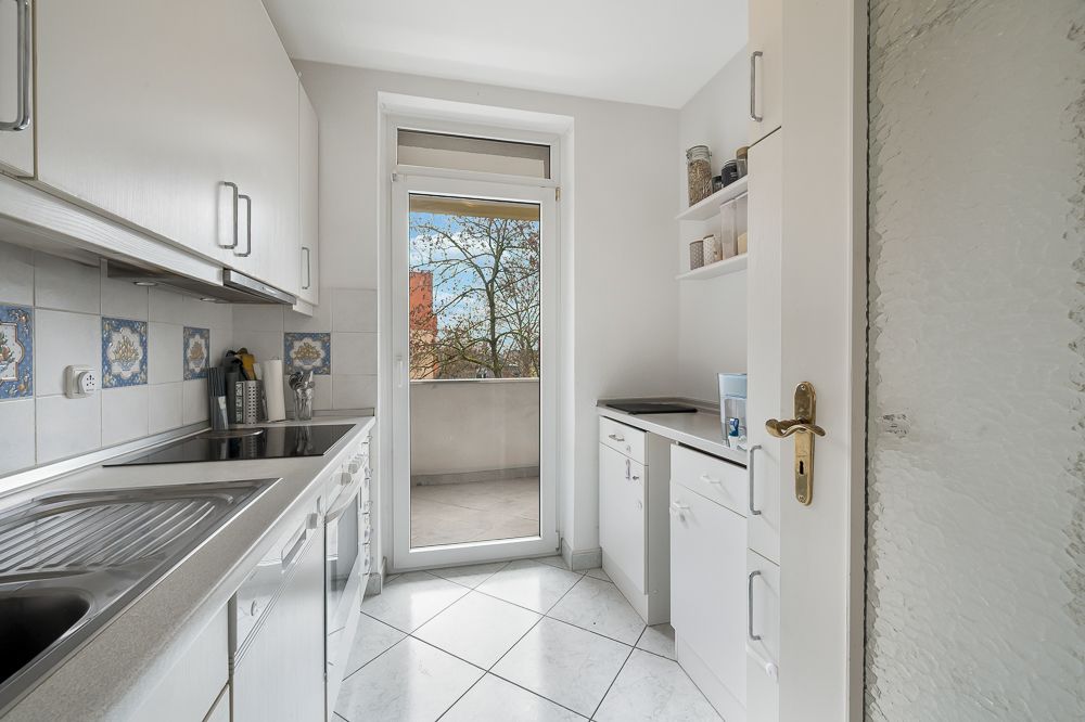 Helle Küche mit weißen Schränken und Zugang zu einem Balkon.