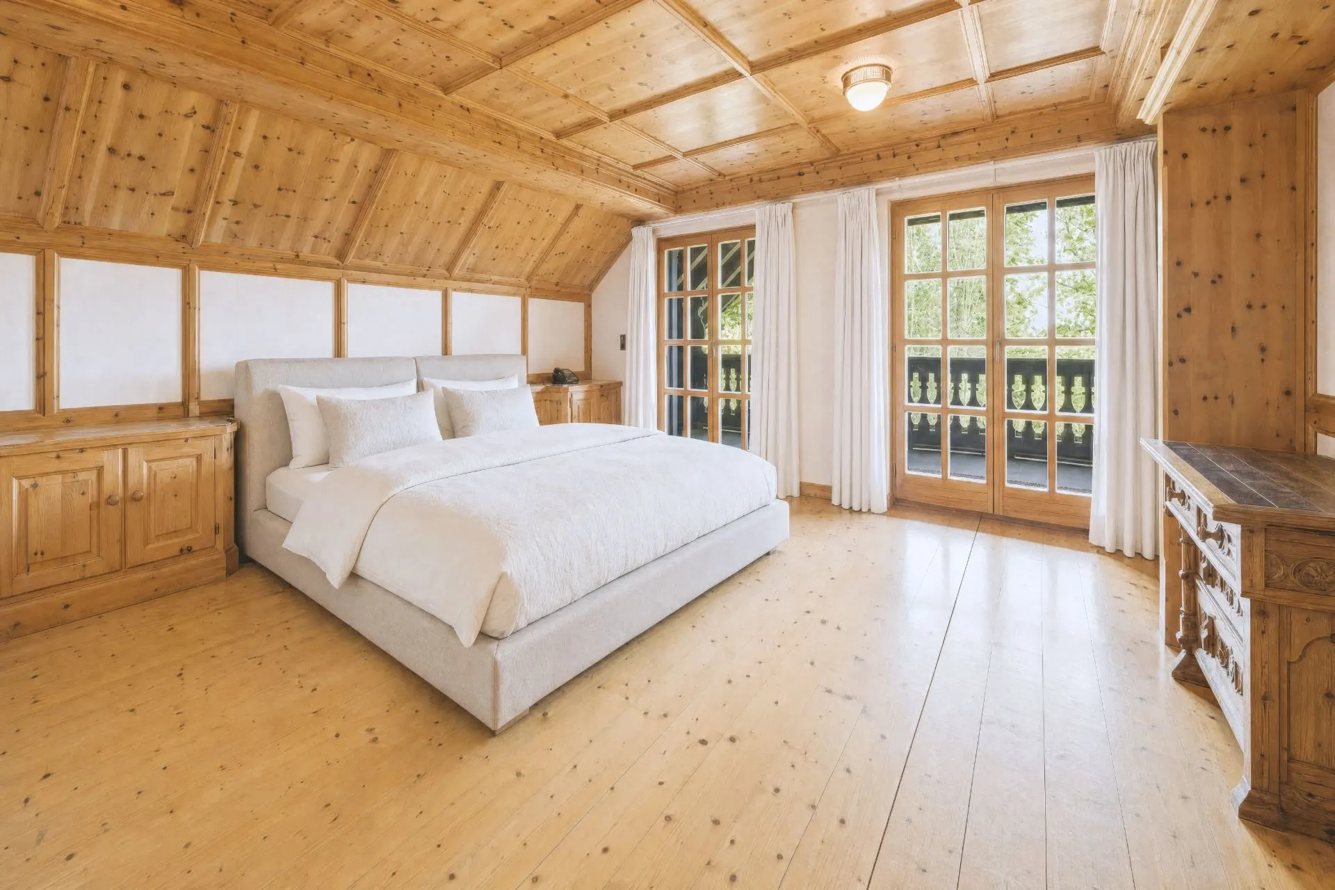 Helles Schlafzimmer mit Holzdecke, Doppelbett, Schränken und Zugang zu einem Balkon.