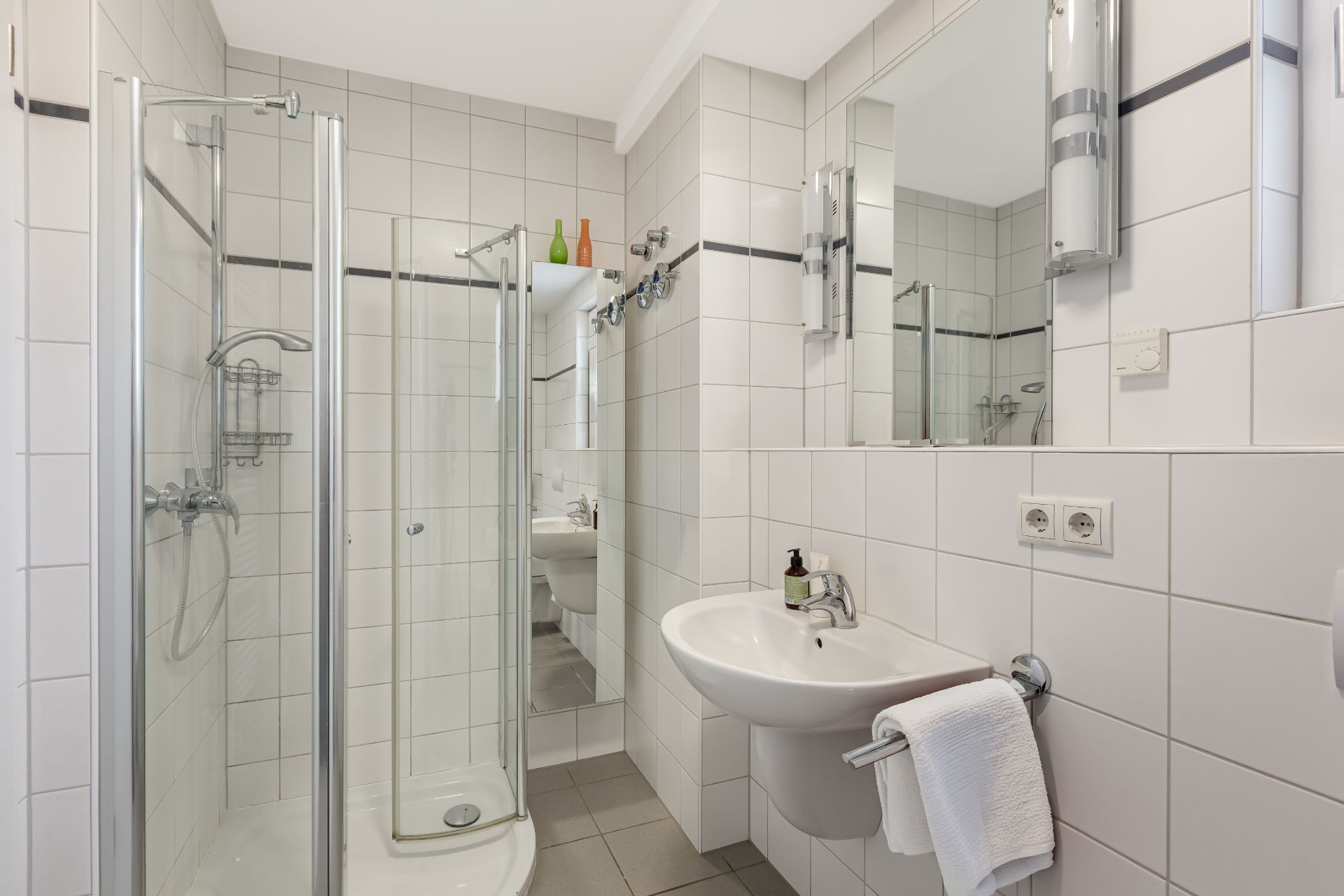 Modernes Badezimmer mit Duschkabine, Waschbecken, Spiegel und weiß gefliesten Wänden.