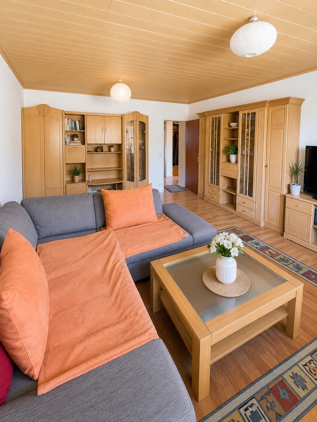 Wohnzimmer mit grauem Sofa, Holzmöbeln und Couchtisch mit Blumenvase.