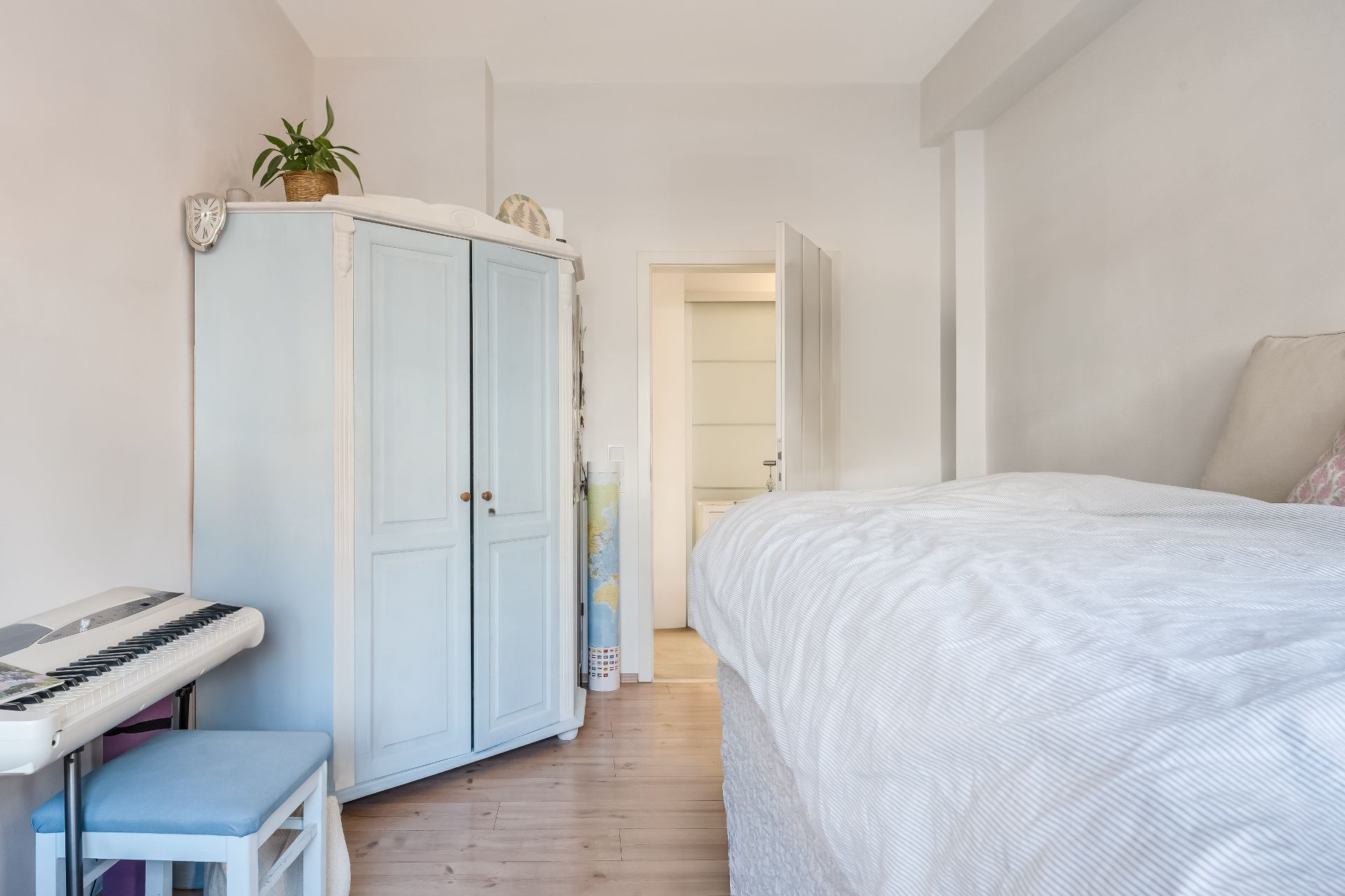Helles Schlafzimmer mit großem Bett, hellblauem Schrank und E-Piano mit Hocker.