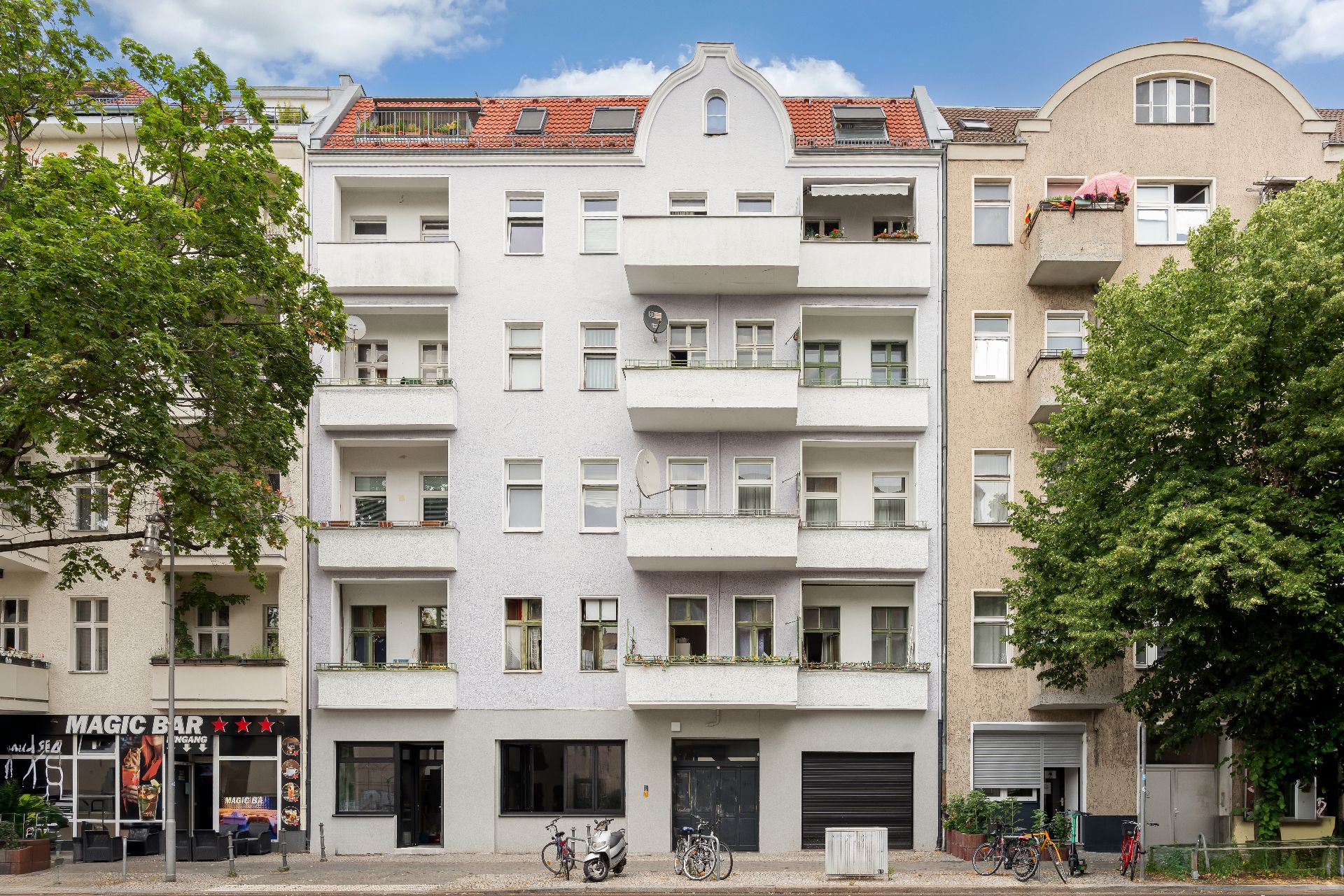 Vorderansicht eines Mehrfamilienhauses mit Balkonen, Bäumen und Fahrrädern davor.