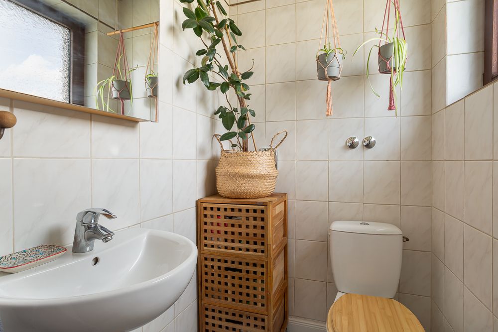 Kleines Badezimmer mit Waschbecken, Toilette, Holzregal und mehreren Pflanzen.