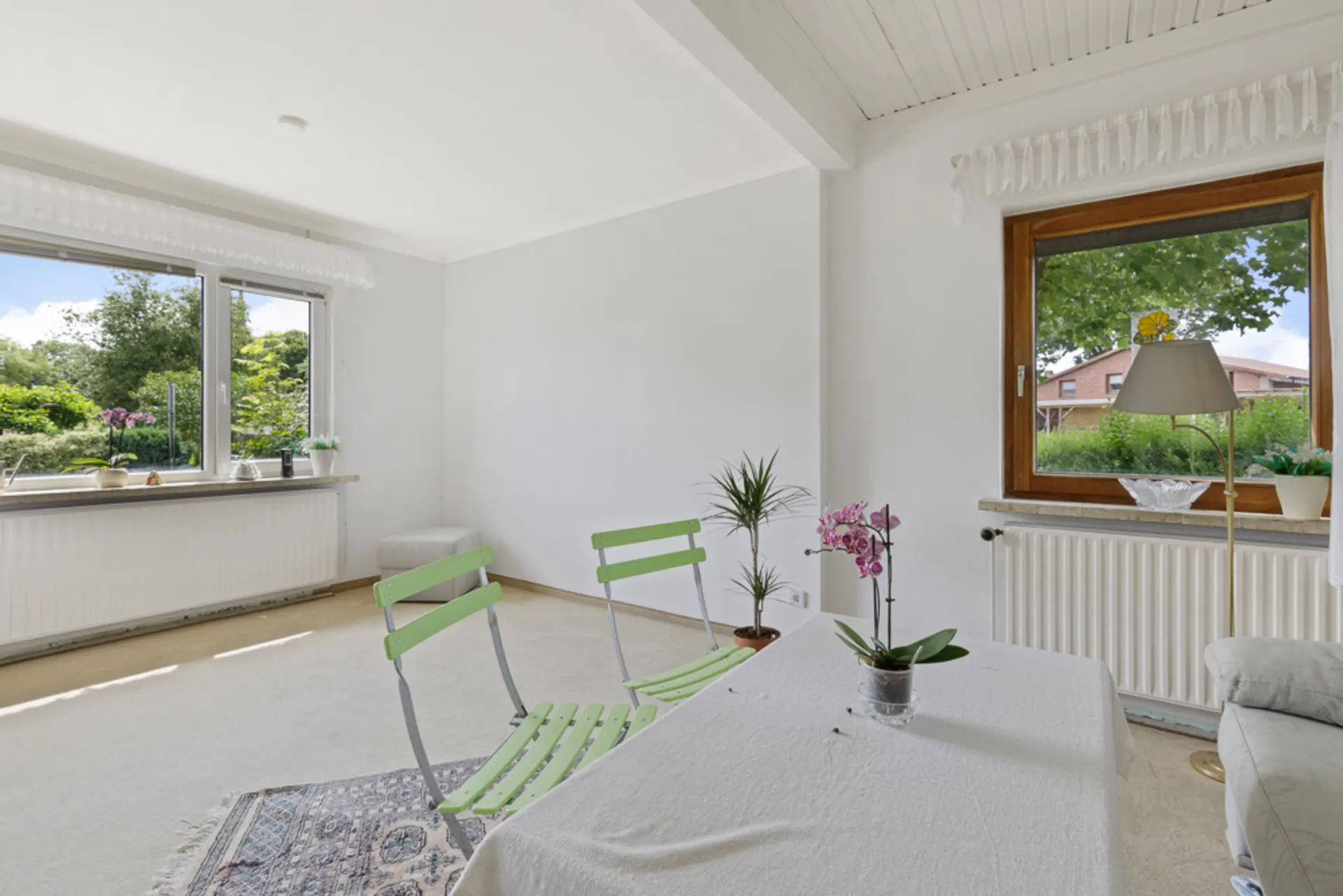 Helles Wohnzimmer mit zwei grünen Stühlen, Tisch, Pflanzen und großen Fenstern mit Blick ins Grüne.