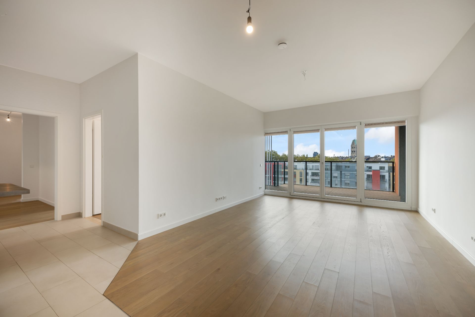 Helles Wohnzimmer mit Parkettboden, großen Fenstern und Zugang zu einem Balkon.