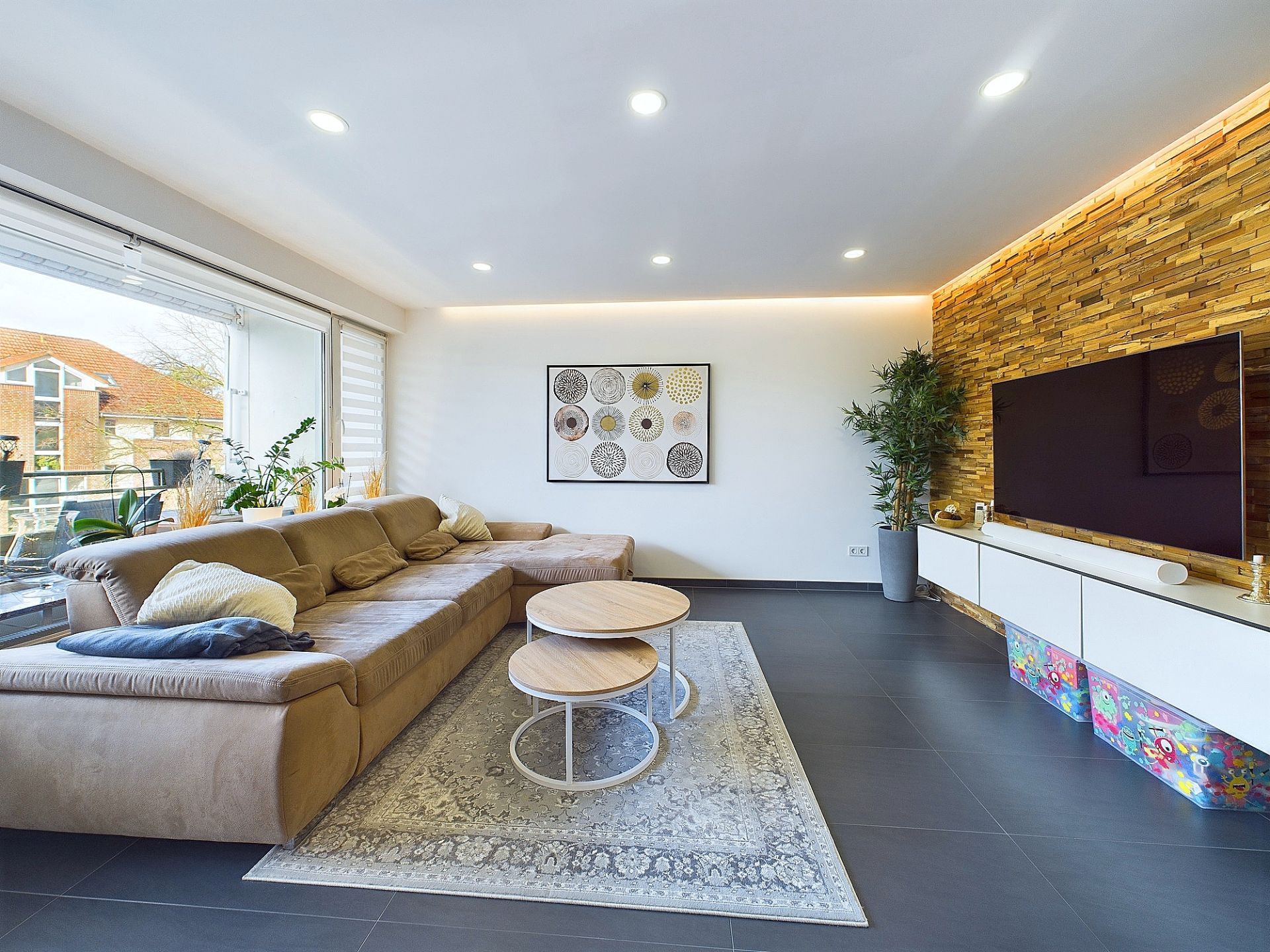 Modernes Wohnzimmer mit großer Eckcouch, Couchtischen, Fernseher und Pflanze.