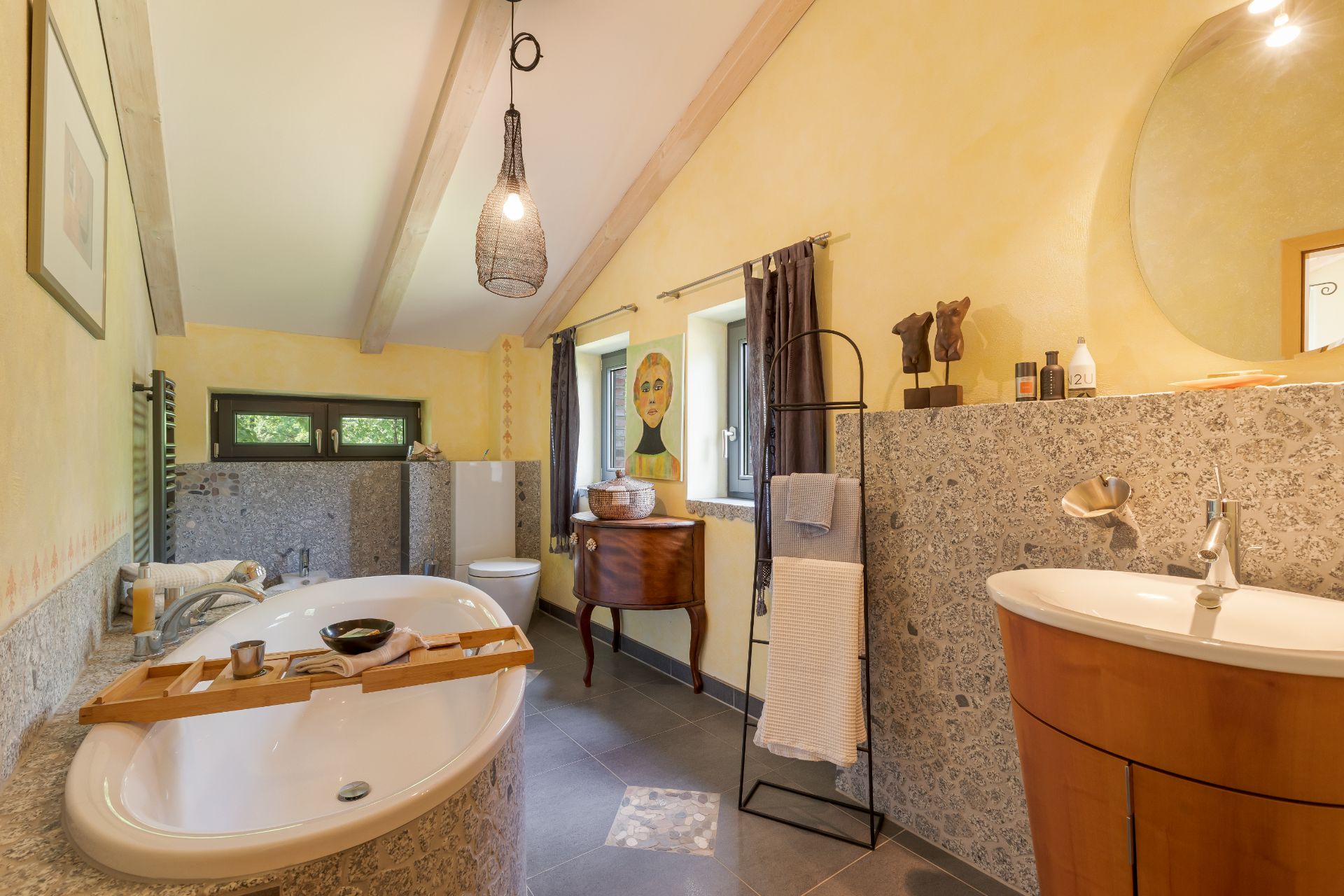 Helles Badezimmer mit freistehender Badewanne, Waschbecken, Toilette und Fenster.