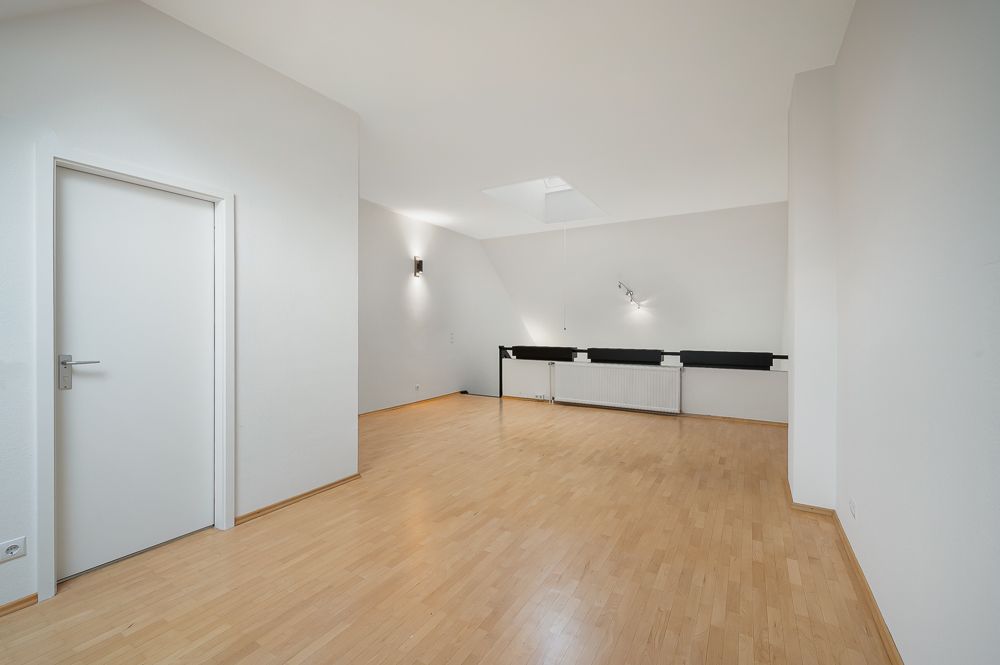 Heller Raum mit Holzfußboden, weißen Wänden, Tür und Deckenleuchten.