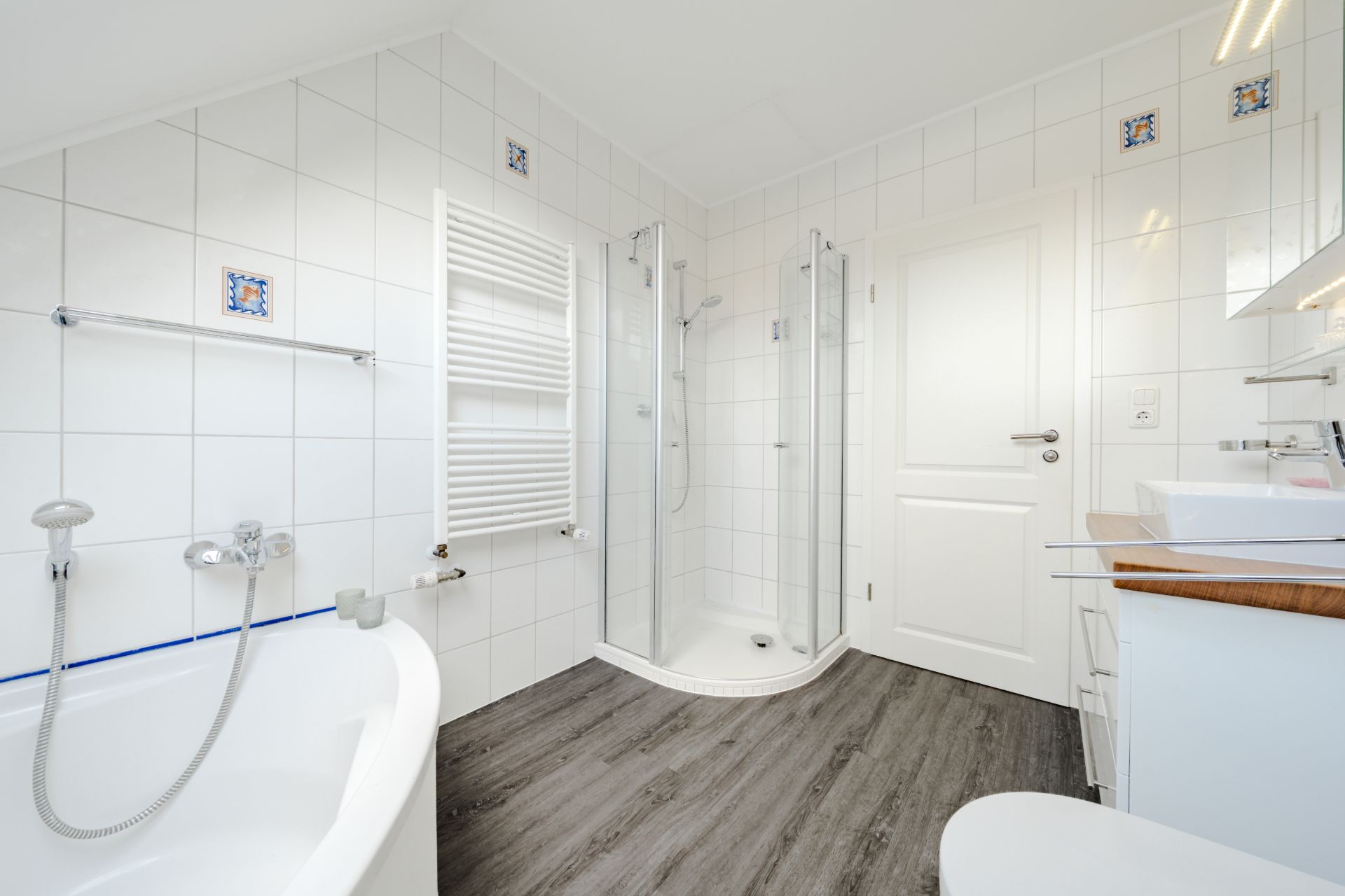 Helles Badezimmer mit Dusche, Badewanne, Waschbecken und weiß gefliesten Wänden.